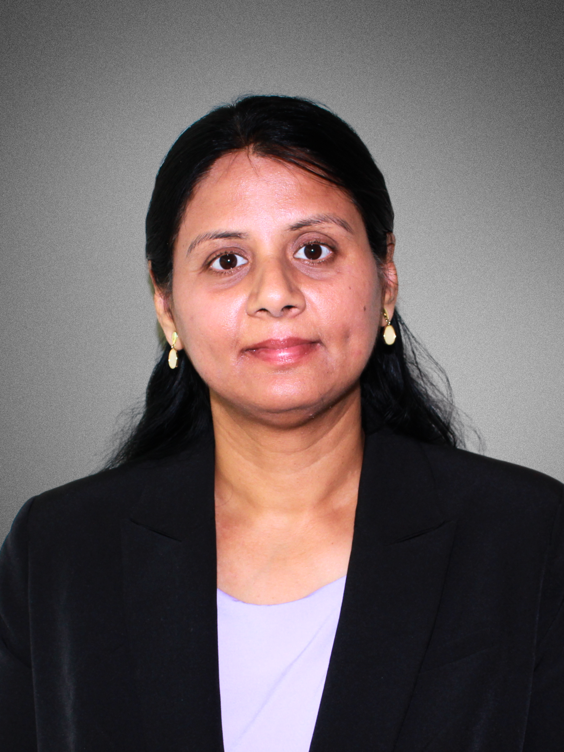 Professional woman with dark hair wearing a black blazer and pearl earrings, posing against a neutral gray background.