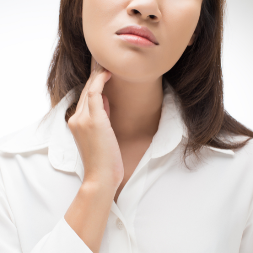 Close-up of a woman with light skin touching her neck, wearing a white collared shirt, against a white background.