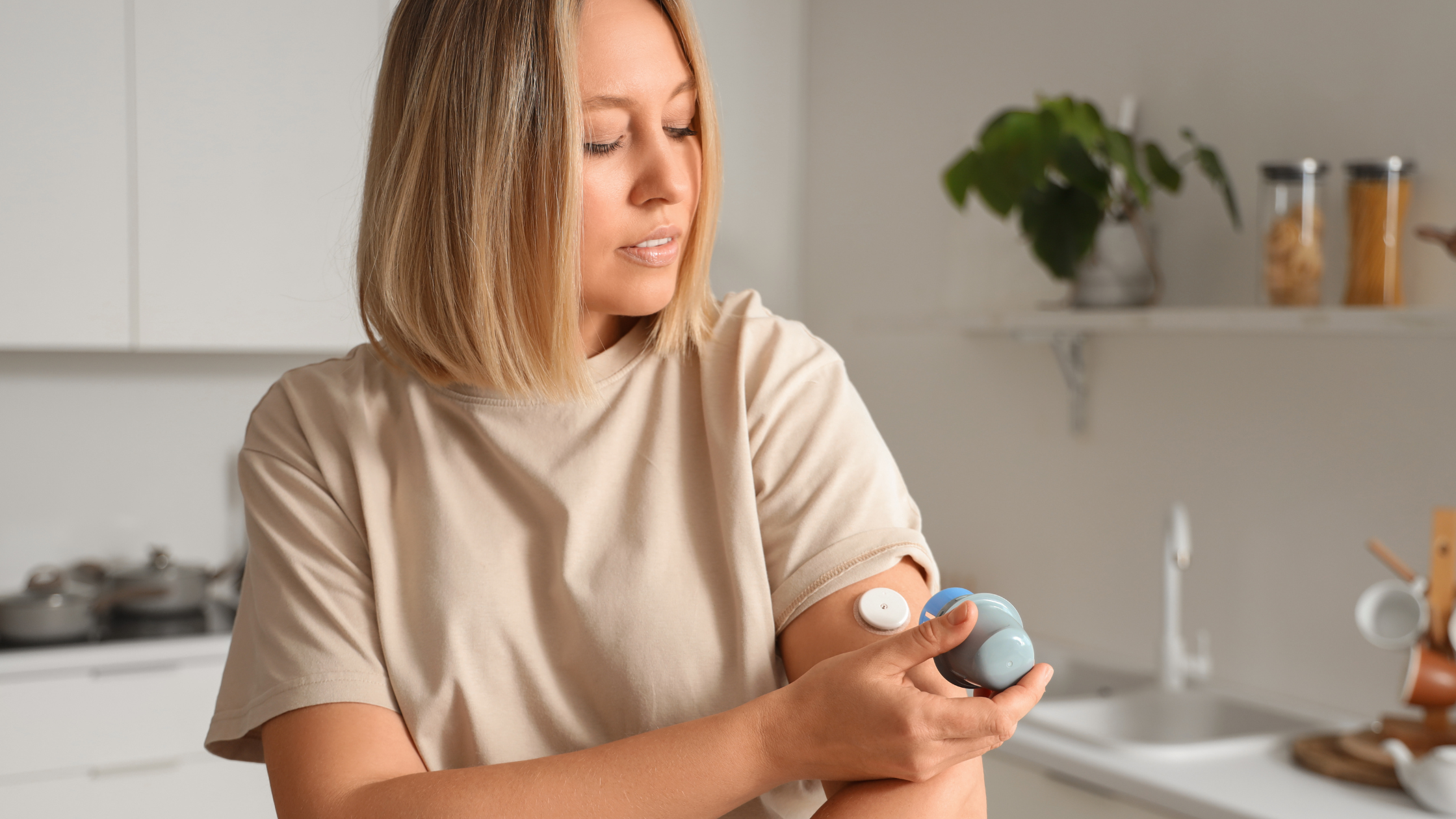 A woman holding a portable electronic device with a patch on her arm in a kitchen.