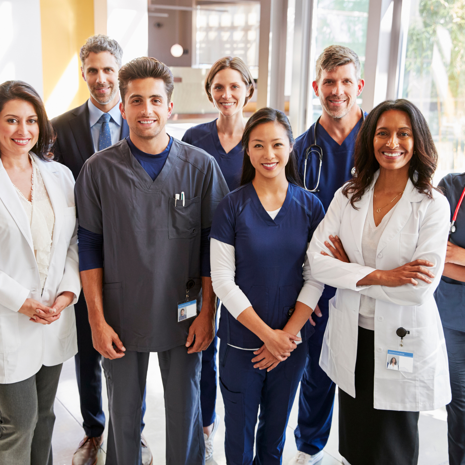Group of diverse healthcare professionals including doctors and nurses standing together in a hospital or clinic, smiling at the camera.