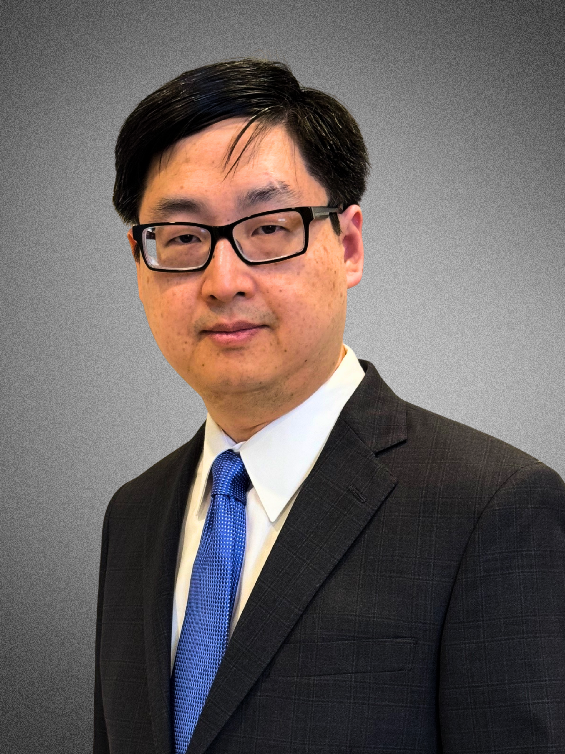 Portrait of a man in a suit and tie wearing glasses, against a plain grey background.