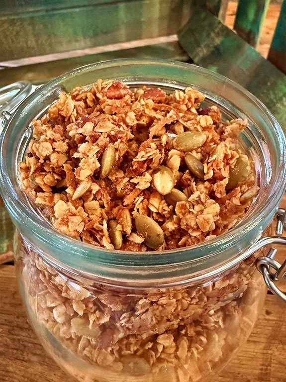 A glass jar filled with homemade granola that contains oats, nuts, honey.