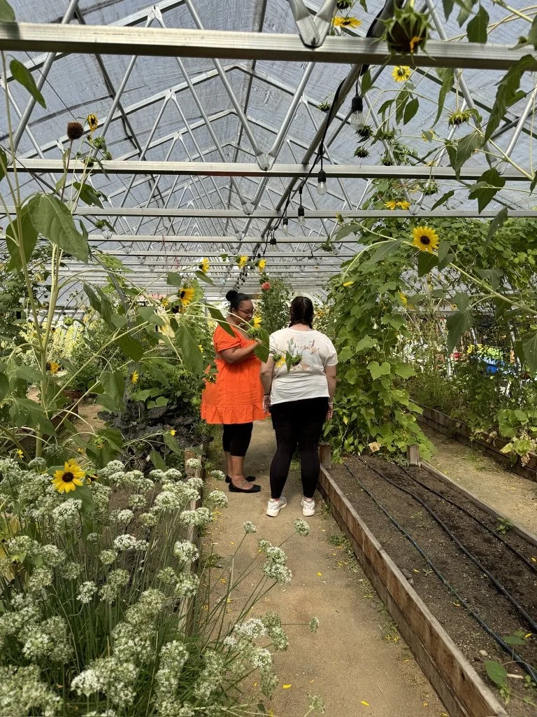 Women-led wellness workshop in Nevada – participants conversing in greenhouse filled with sunflowers and plants facilitated by ALIGN Agency