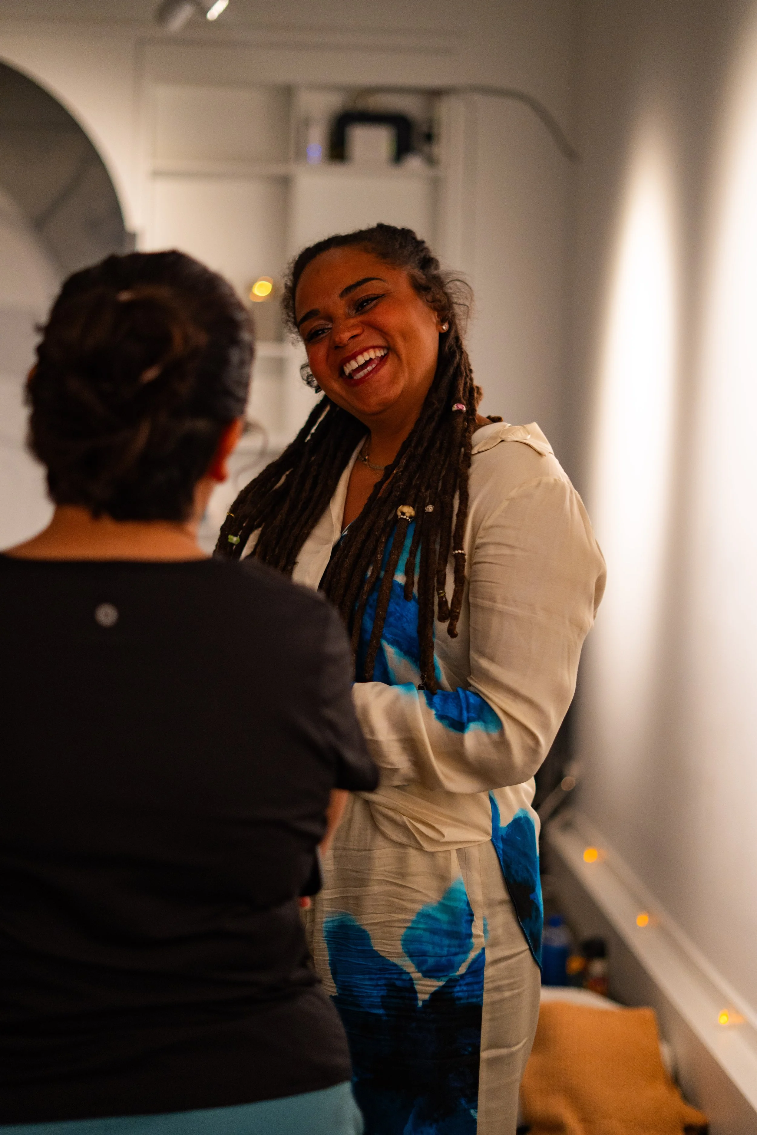 Indoor wellness or coaching workshop for organizations in Nevada – two women engaged in conversation, smiling, one with dark hair in black top and the other with braided hair in beige and blue patterned outfit, facilitated by ALIGN Agency