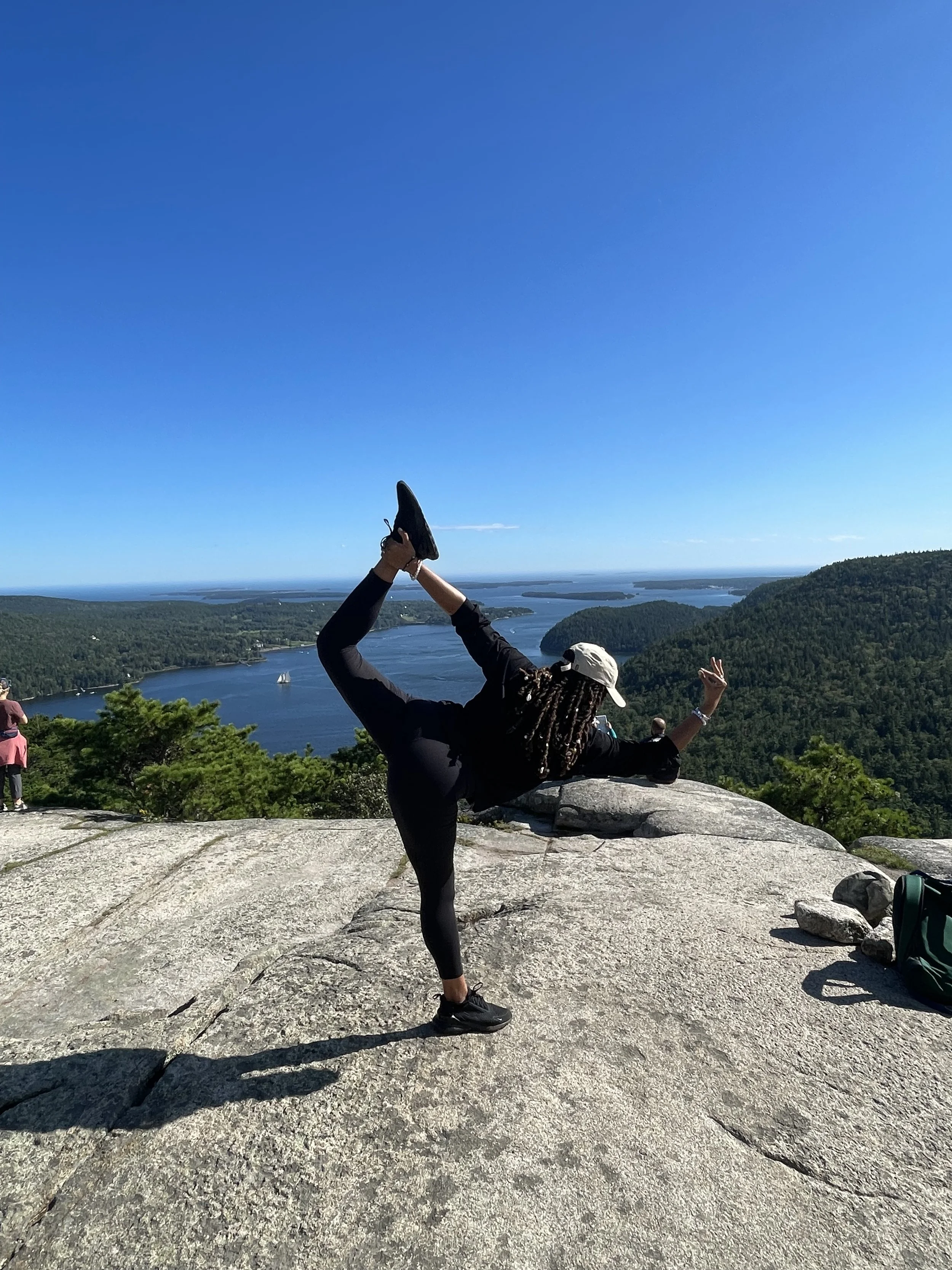 Outdoor yoga session for wellness workshops in Nevada – woman practicing yoga on large rock with scenic lake and forest view in background, facilitated by ALIGN Agency
