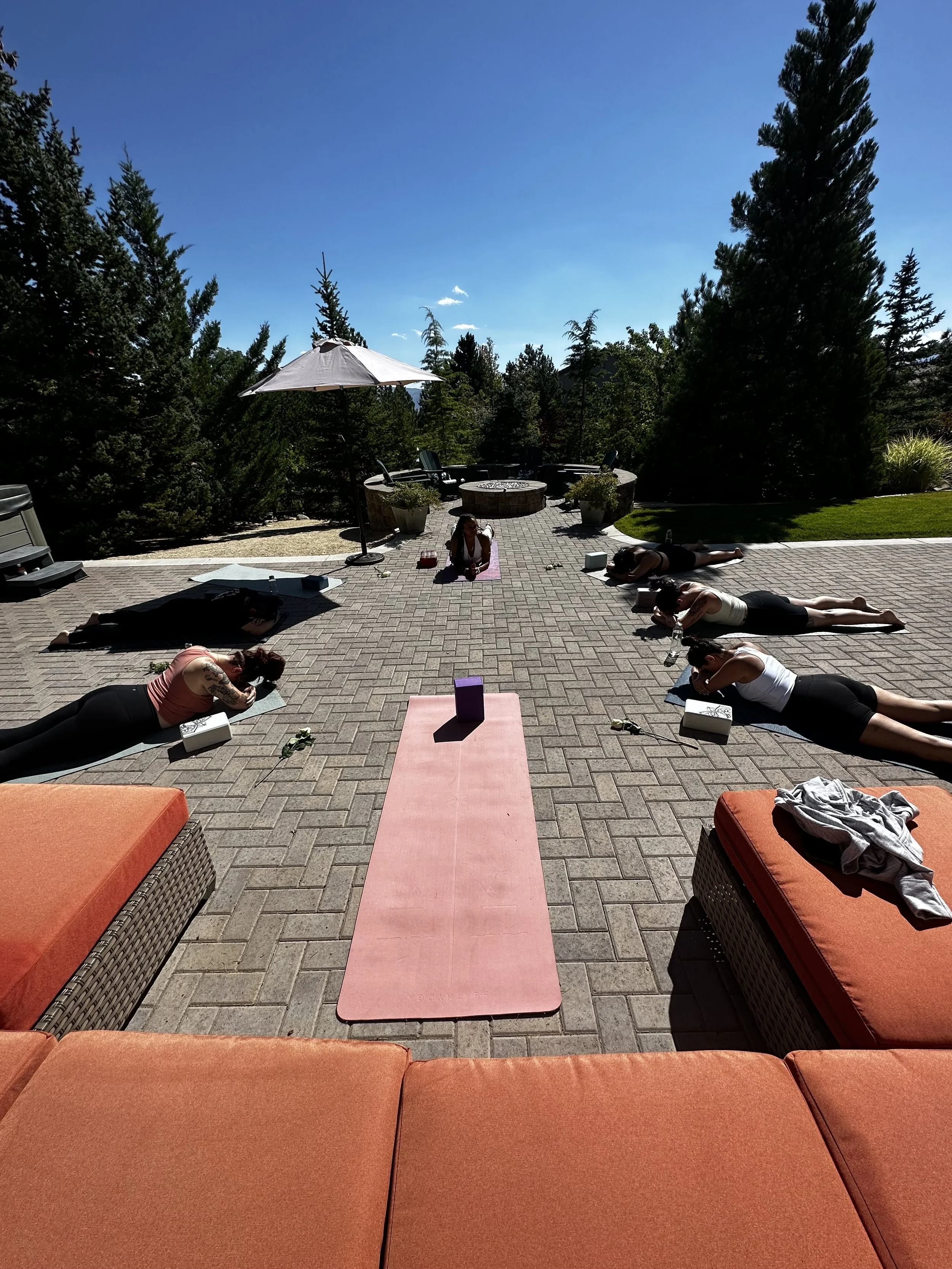 Outdoor yoga session for wellness workshops in Nevada – participants lying on yoga mats on patio surrounded by trees and outdoor furniture, facilitated by ALIGN Agency