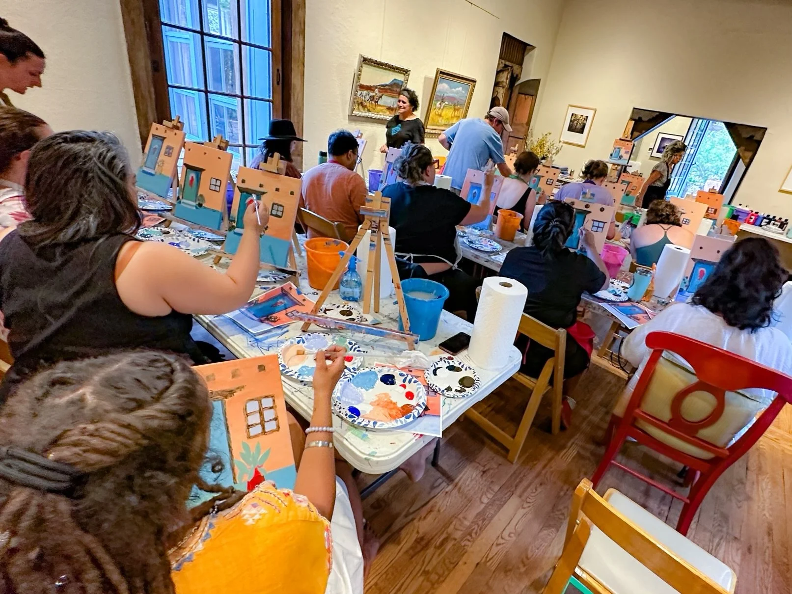 People participating in a house painting workshop in an art studio, creating miniature house paintings on canvases.