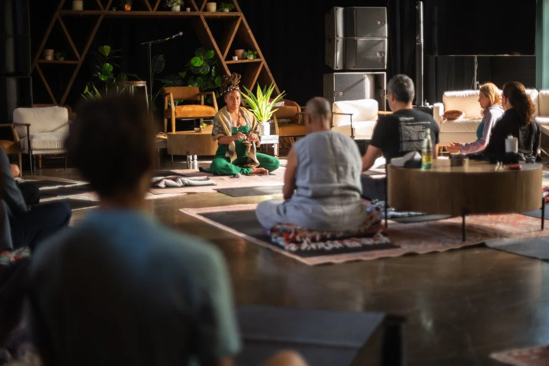Indoor wellness or meditation workshop for mission-driven organizations in Nevada – woman dressed in green and gold leading yoga or meditation session with small group seated on floor and cushions, facilitated by ALIGN Agency
