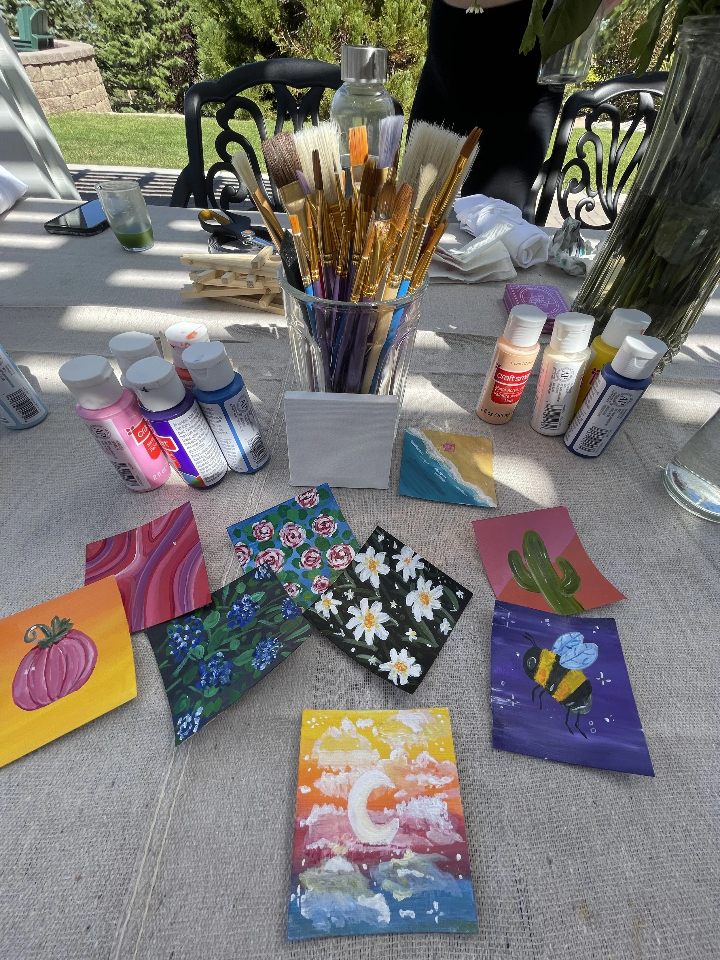 Creative wellness workshop for mission-driven organizations in Nevada – table with paint supplies, brushes, and small painted artworks including pumpkin, flowers, whale, bee, cactus, and sunset with crescent moon, facilitated by ALIGN Agency