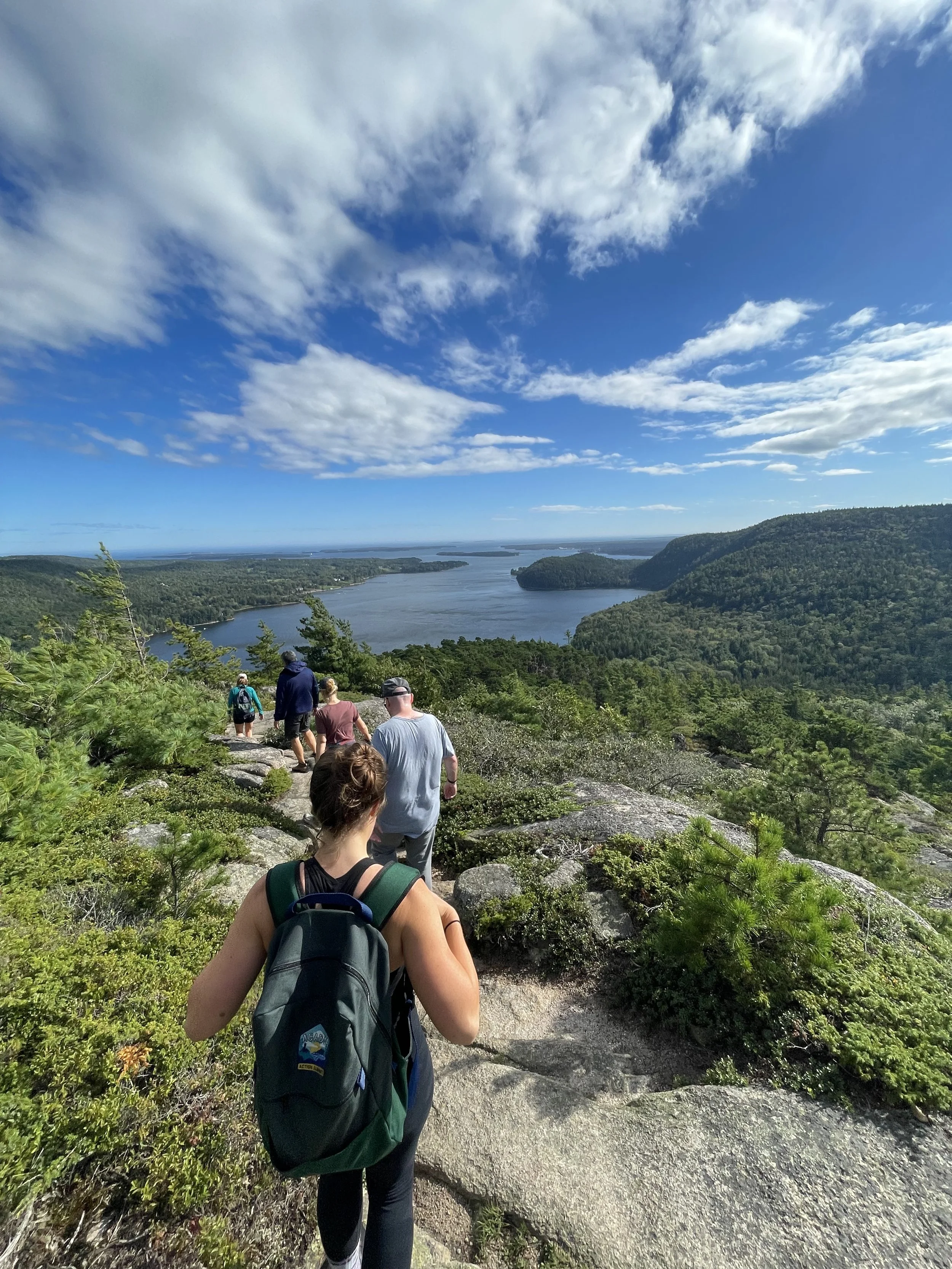 Outdoor wellness and team-building workshop for mission-driven organizations in Nevada – hikers walking on trail overlooking large body of water and lush green hills under partly cloudy sky, facilitated by ALIGN Agency