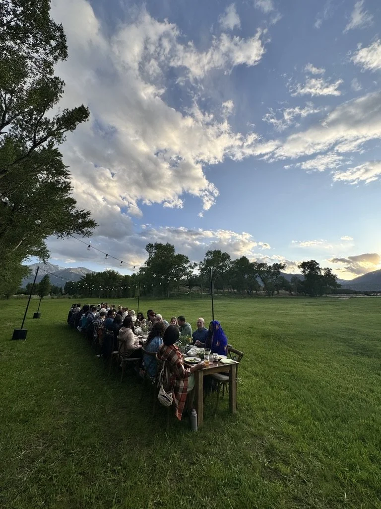 Outdoor wellness or community event for mission-driven organizations in Nevada – long dinner table with participants set in large green field under partly cloudy sky, facilitated by ALIGN Agency
