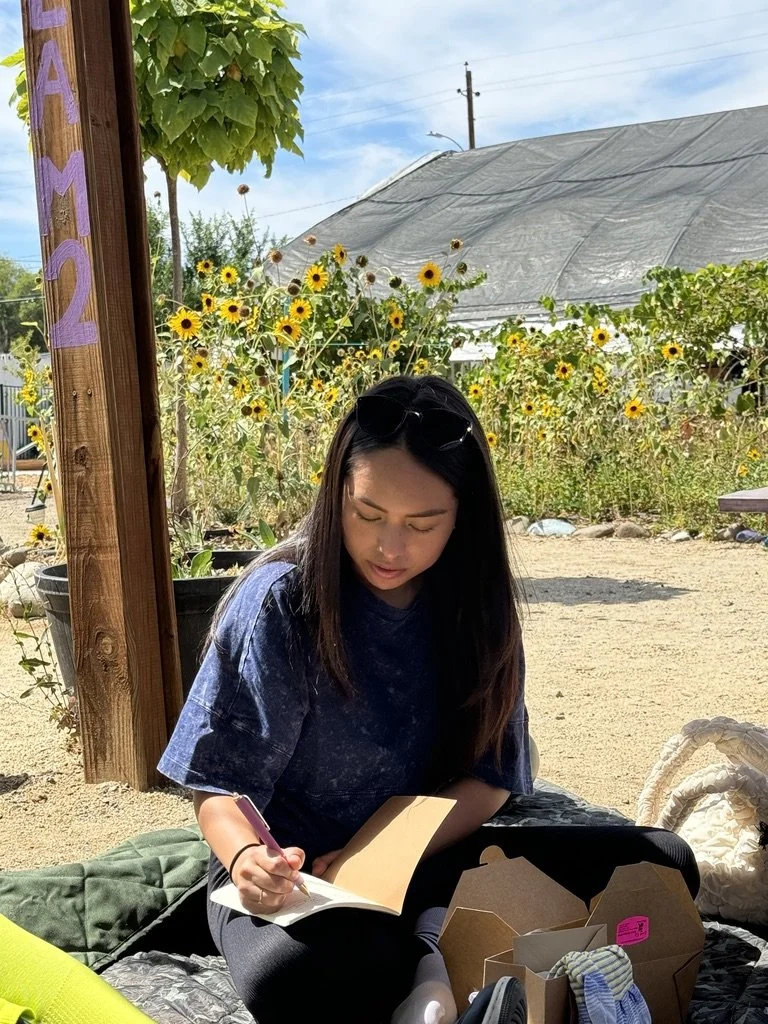 Outdoor creative wellness workshop for mission-driven organizations in Las Vegas – participant journaling near sunflower garden and greenhouse facilitated by ALIGN Agency