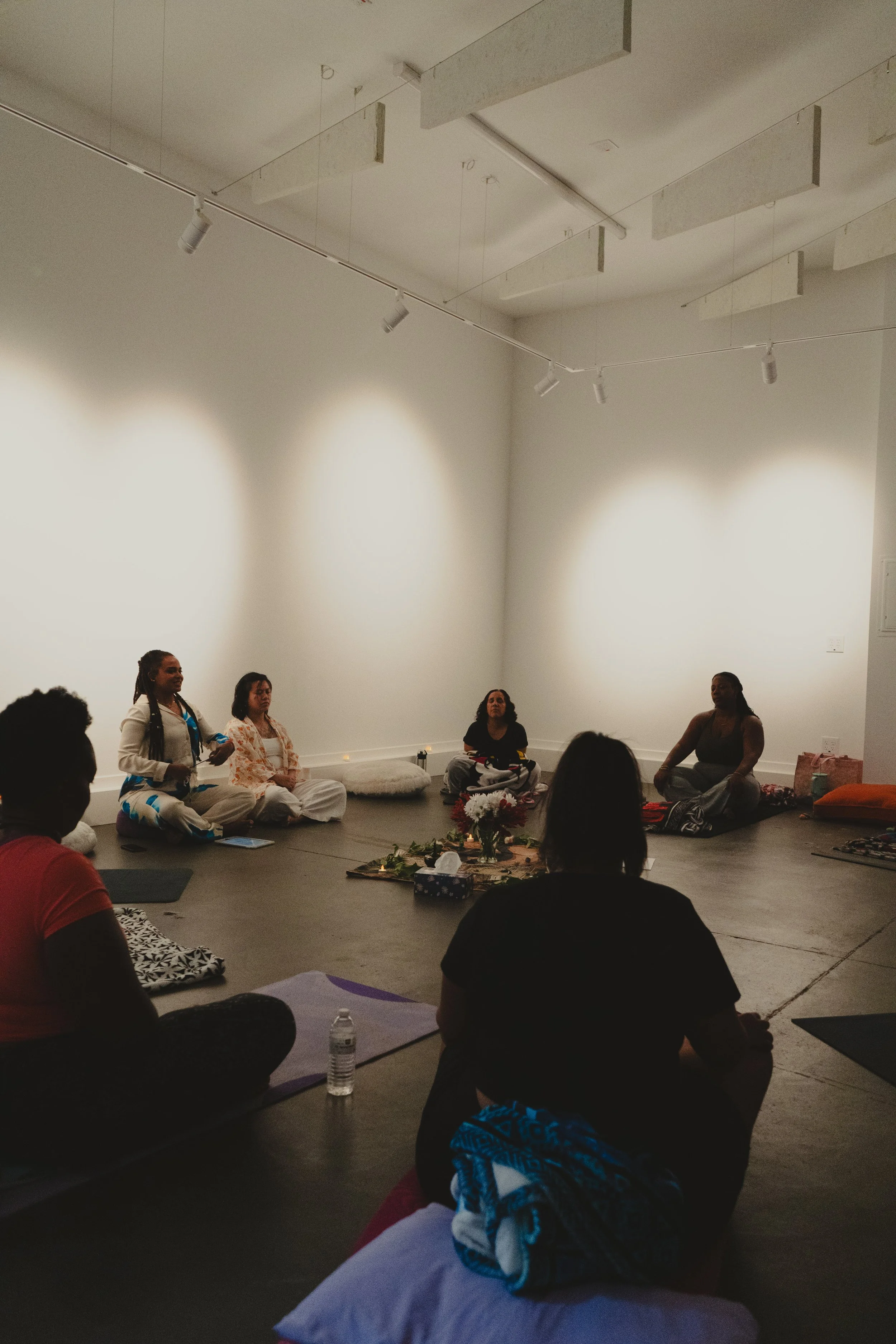 Indoor wellness or mindfulness workshop for mission-driven organizations in Nevada – participants seated in circle on yoga mats and cushions in calm, well-lit room with central arrangement of flowers and candles, facilitated by ALIGN Agency