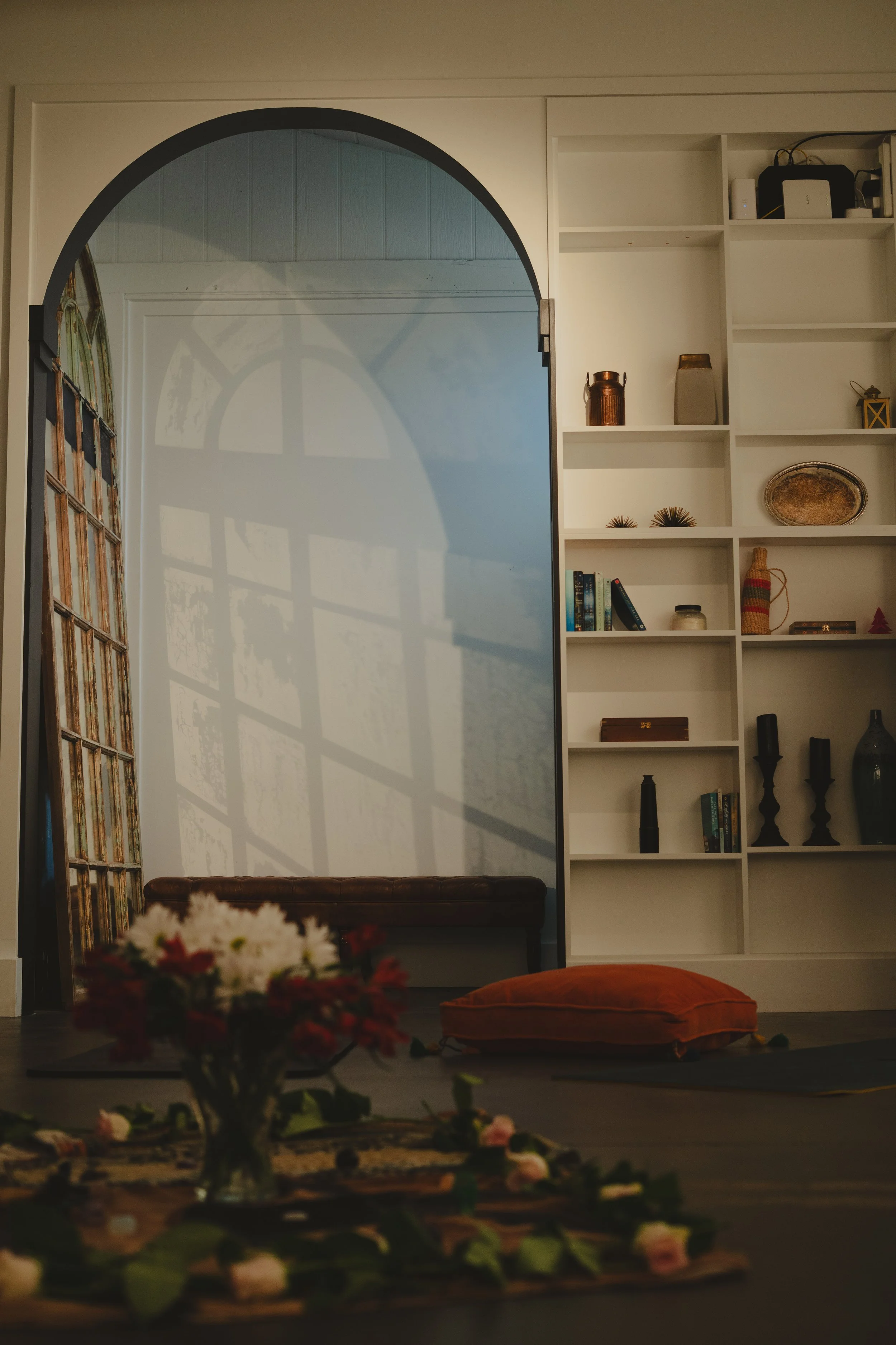Indoor wellness or retreat workshop space for mission-driven organizations in Nevada – cozy room with large arched mirror reflecting sunlight, decorated with books, candles, shelves, and floral arrangements, facilitated by ALIGN Agency