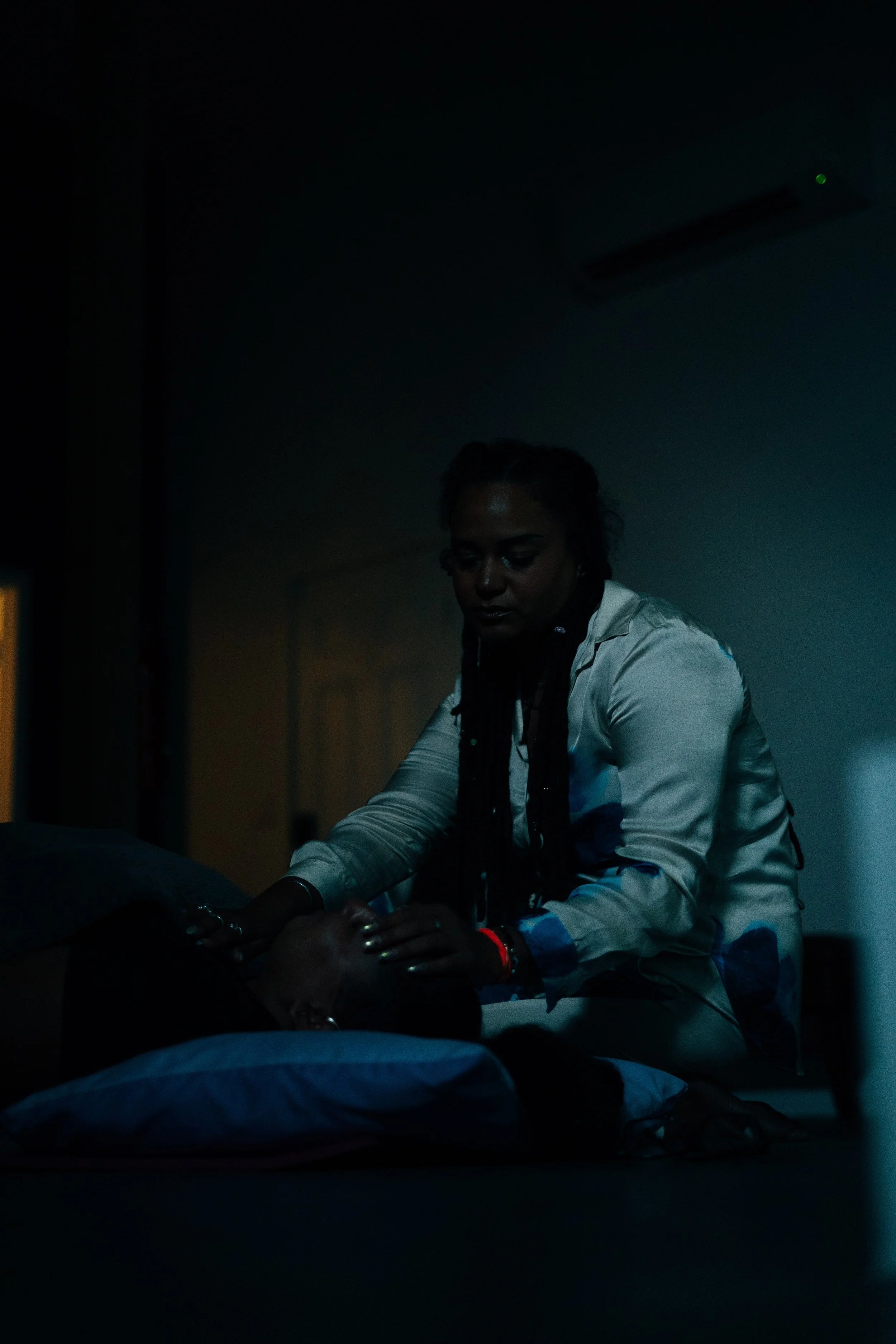 Trauma-informed wellness session for mission-driven organizations in Nevada – woman gently holding participant's head while lying on pillow in dimly lit room, facilitated by ALIGN Agency