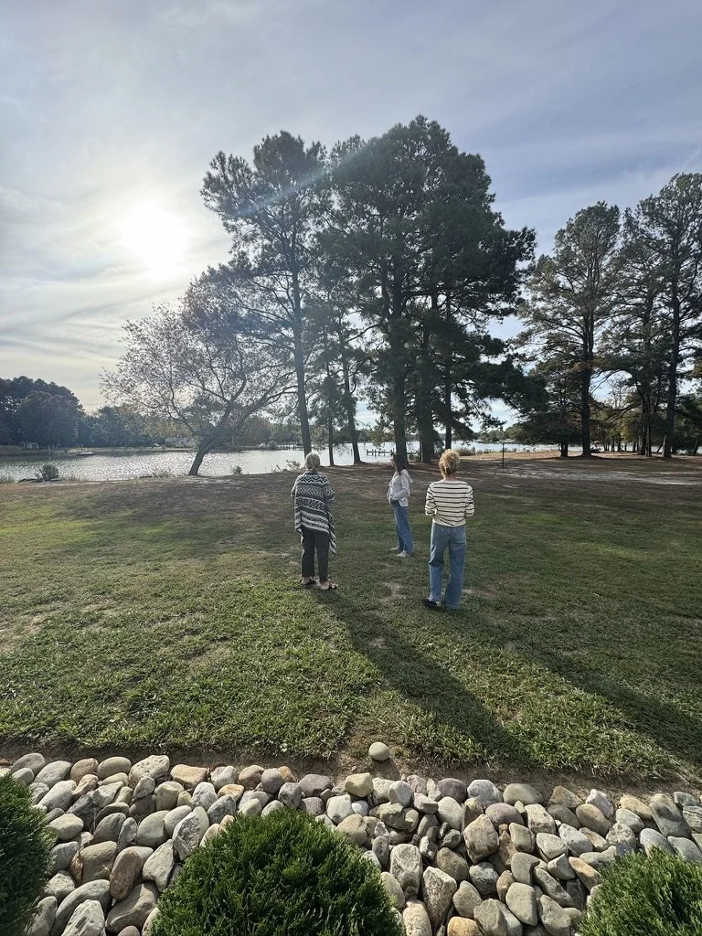 Outdoor wellness or retreat workshop for mission-driven organizations in Nevada – three participants standing on grassy lawn near lake with trees, rocks, and cloudy sky facilitated by ALIGN Agency