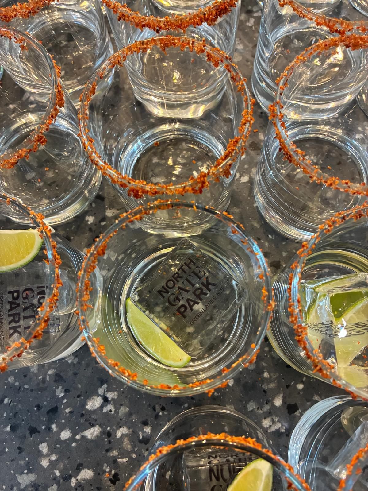 Multiple empty tequila glasses with salted rims and lime wedges inside some glasses, arranged on a granite countertop. Themed event planning, with personalised drinks and ice cubes.