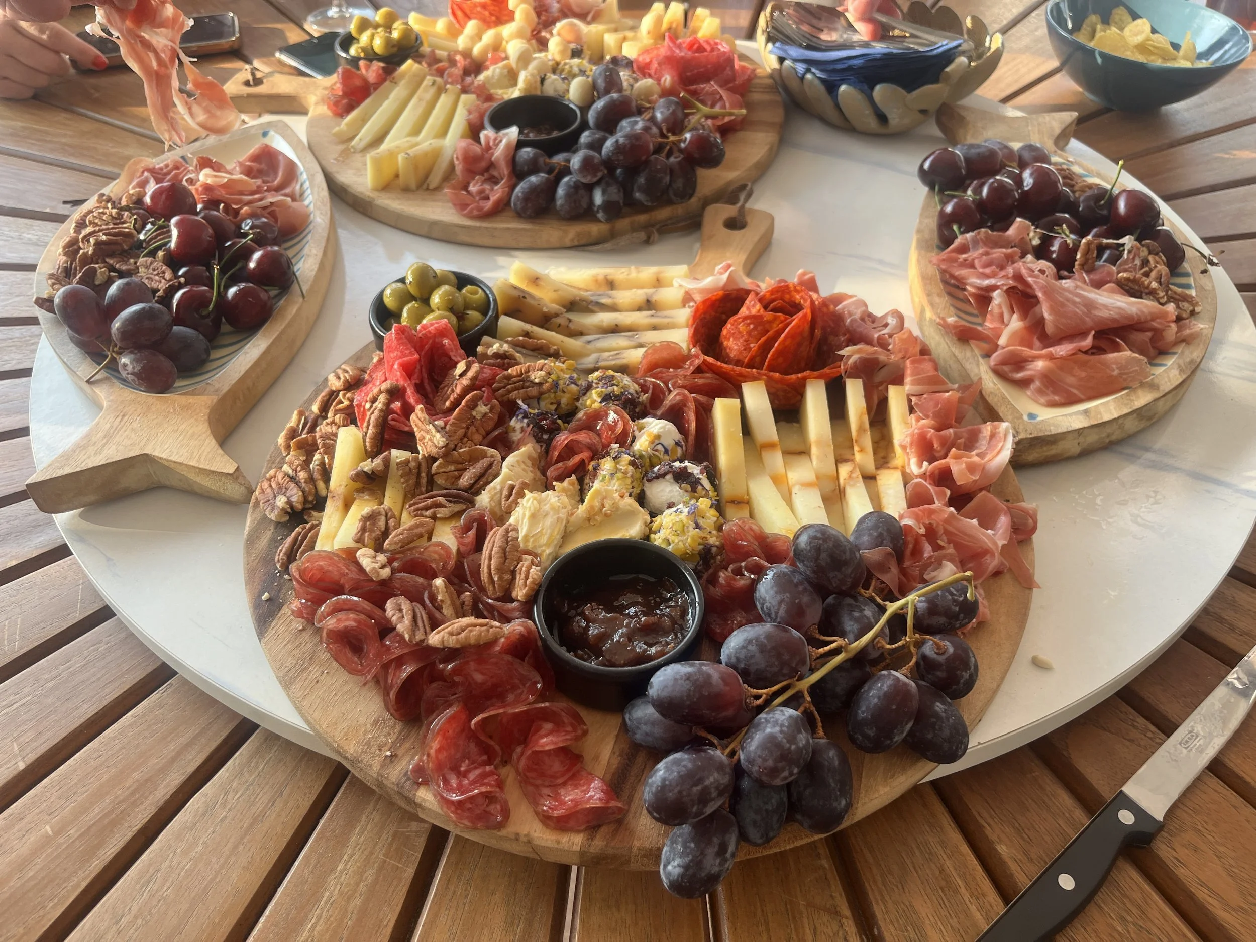 Charcuterie board with cheeses, grapes, cured meats, nuts, and dips on a round table. Themed event planning.