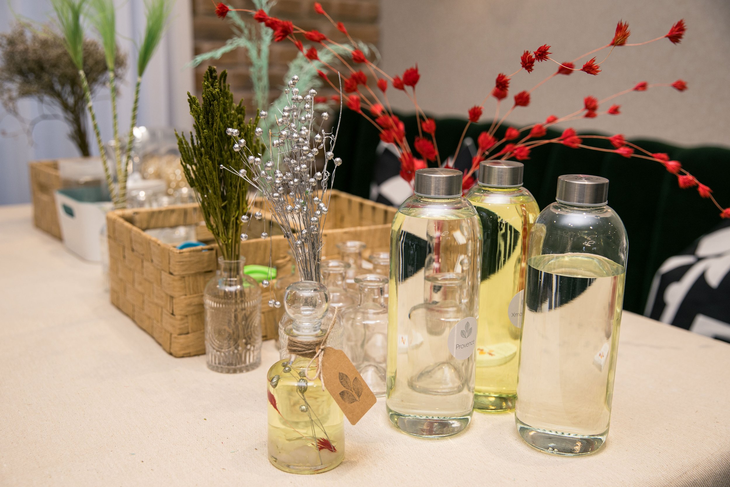 Assortment of glass bottles with liquid and various floral decorations on a beige table. Themed event planning, for diffuser making.