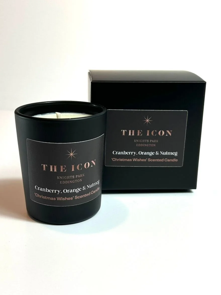 Black scented candle labeled 'The Icon' with cranberry, orange, and nutmeg scent, placed next to its black box. Personalised candle for corporate events.
