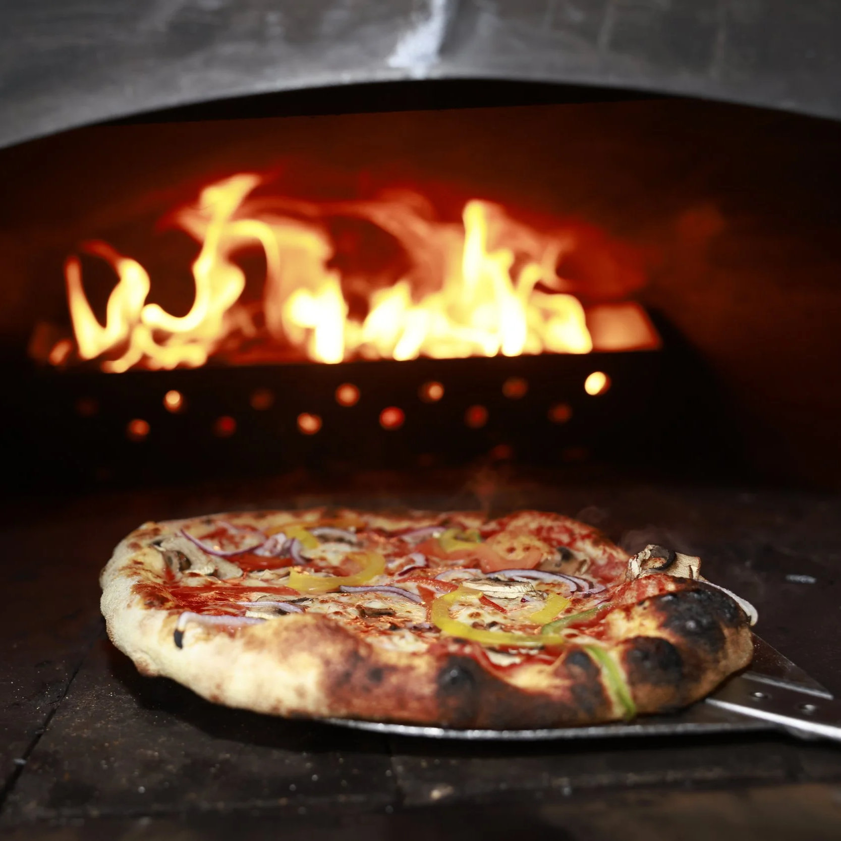 A pizza inside a wood-fired oven with flames burning above.