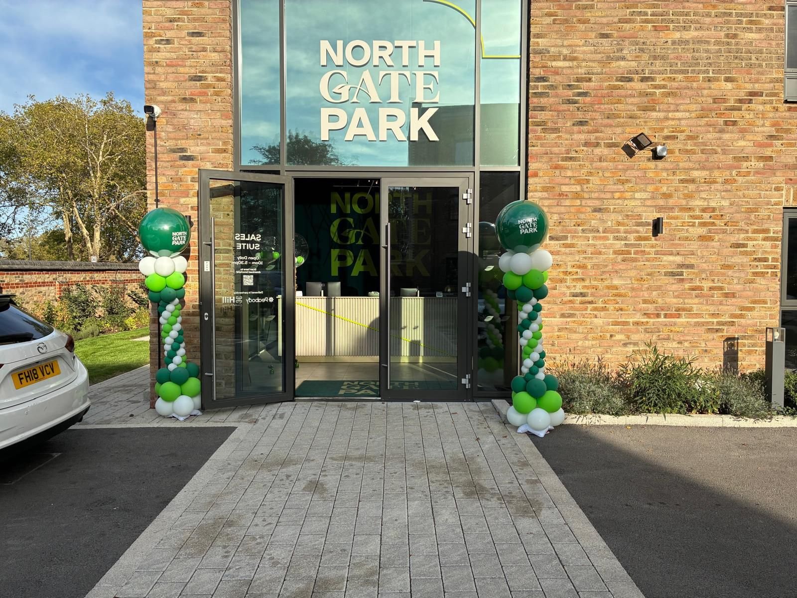 The entrance to North Gate Park building with glass doors, decorated with green, white, and darker green balloons on both sides. Personalised event accessories and stationery.