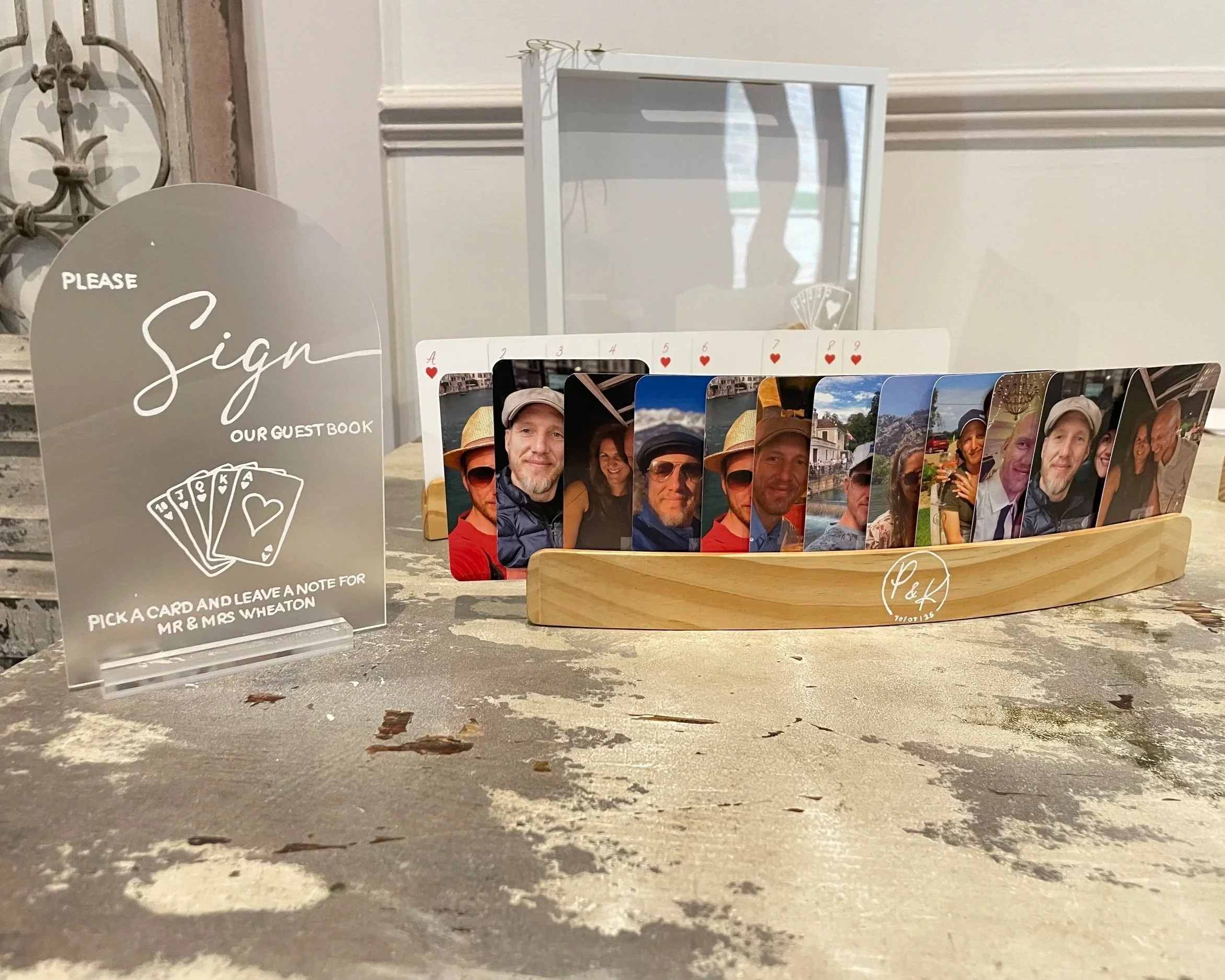 A sign requesting guests to pick a card and leave a note for Mr. and Mrs. Wheaton, next to a wooden display holding various personal photographs of a couple. Personalised event stationery for weddings and events.
