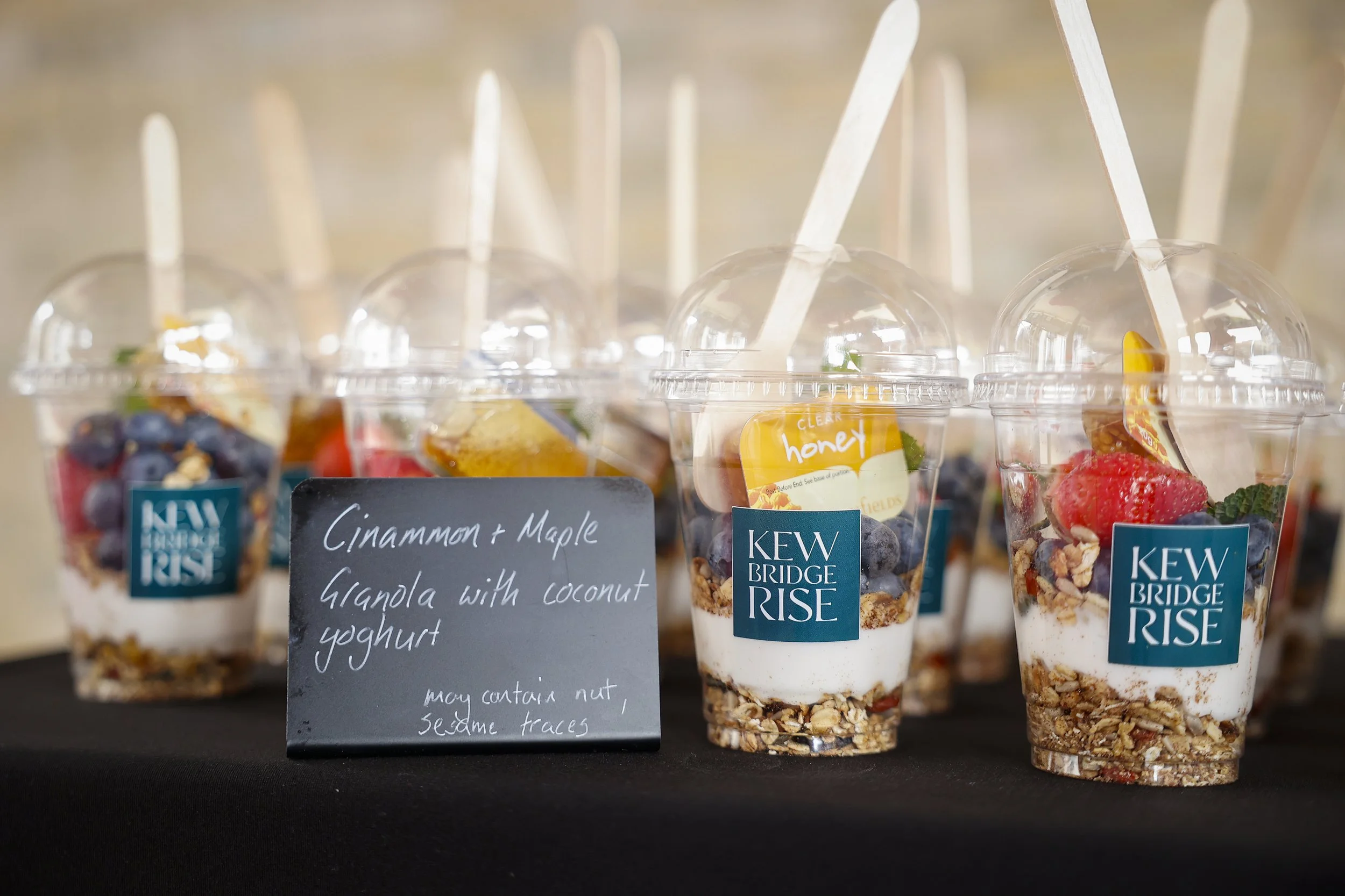 Display of Kew Bridge Rise yogurt parfaits with granola, berries, and honey, labeled with a chalkboard sign.  Themed event planning, stationery and accessories.