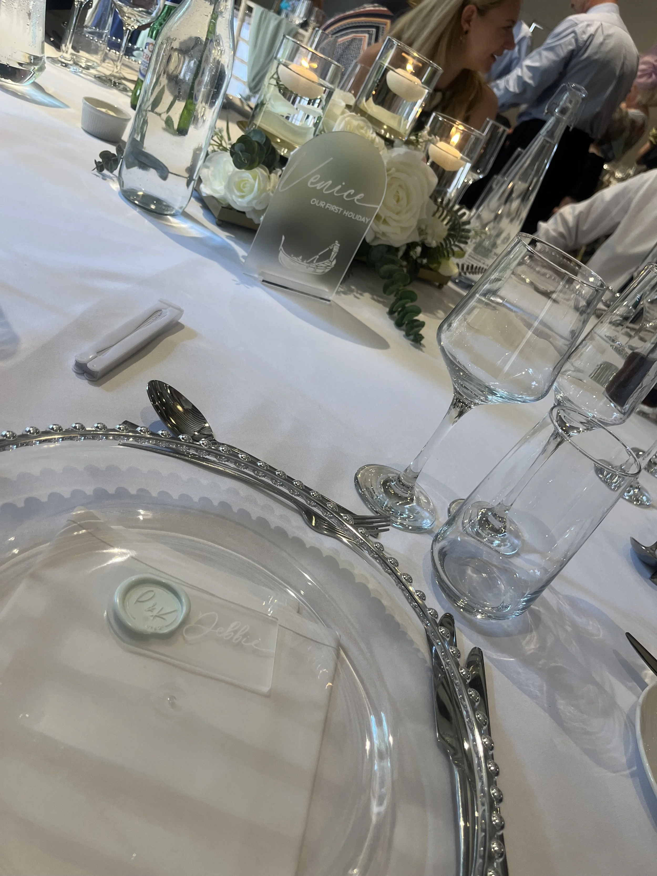 Table setting for a formal event with a faux flower centerpiece with white roses and candles, personalised name plaque and acrylic table sign which has been personalised. Personalised event stationery for weddings and events.