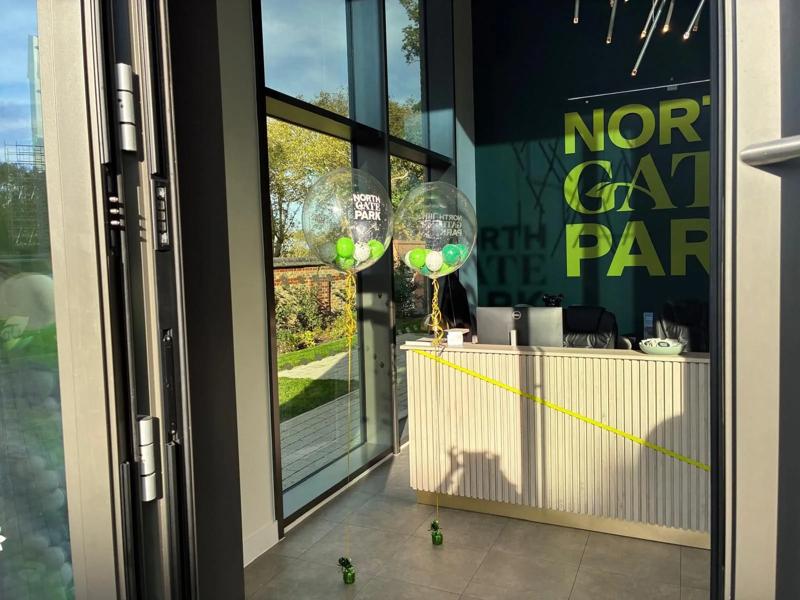 Entrance of Northgate Park with two transparent balloons filled with green and white balls, and yellow ribbons tied to small green weights on floors. Personalised event accessories for events.