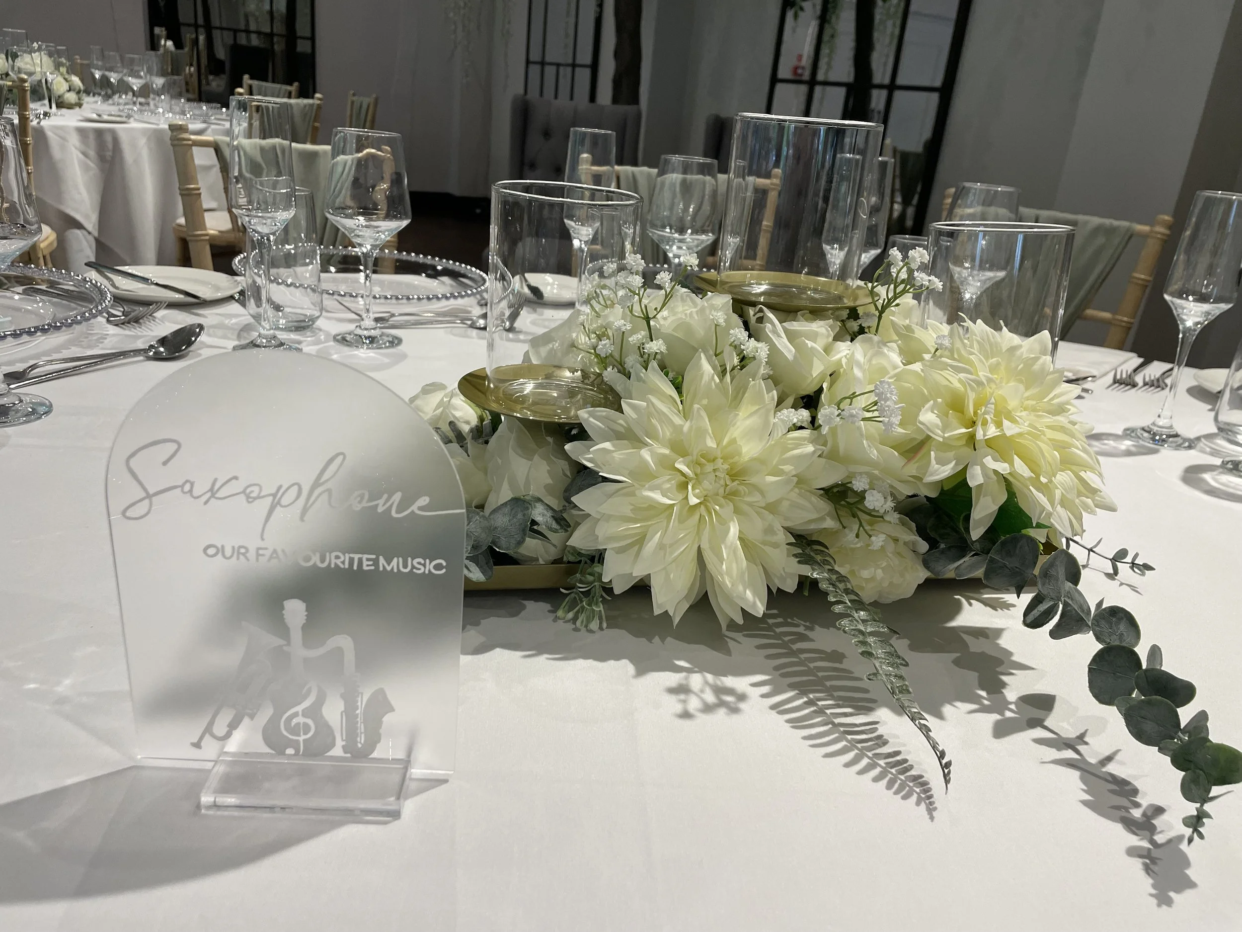 Table decorated with white flowers, including dahlias and roses, with multiple wine glasses and silverware set for a formal event.