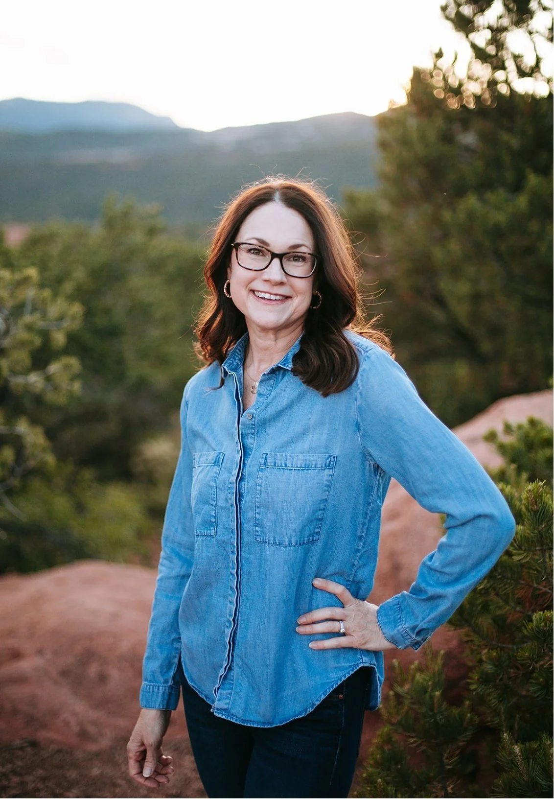 Celia Sugg, Colorado Springs therapist, standing outdoors with mountains and trees in the background.