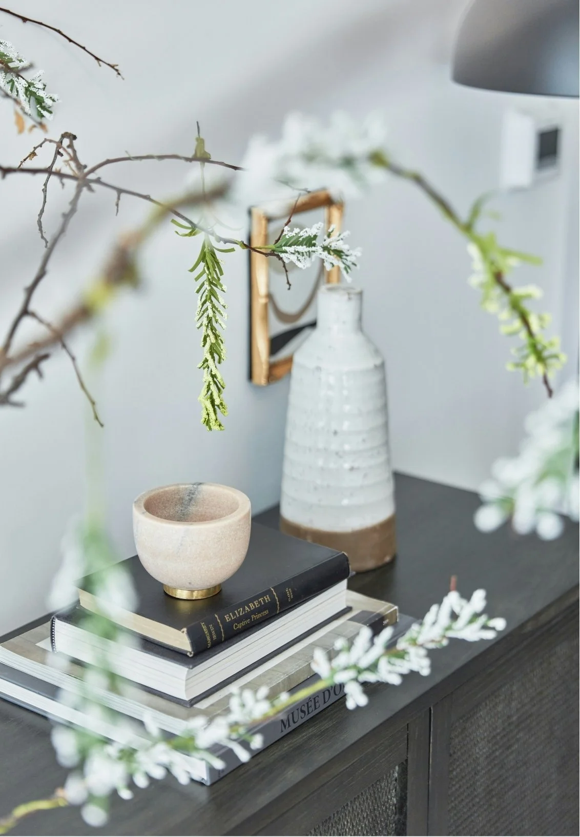 Decorative interior table with a vase, books, a ceramic bowl, and some branches with green and white leaves.