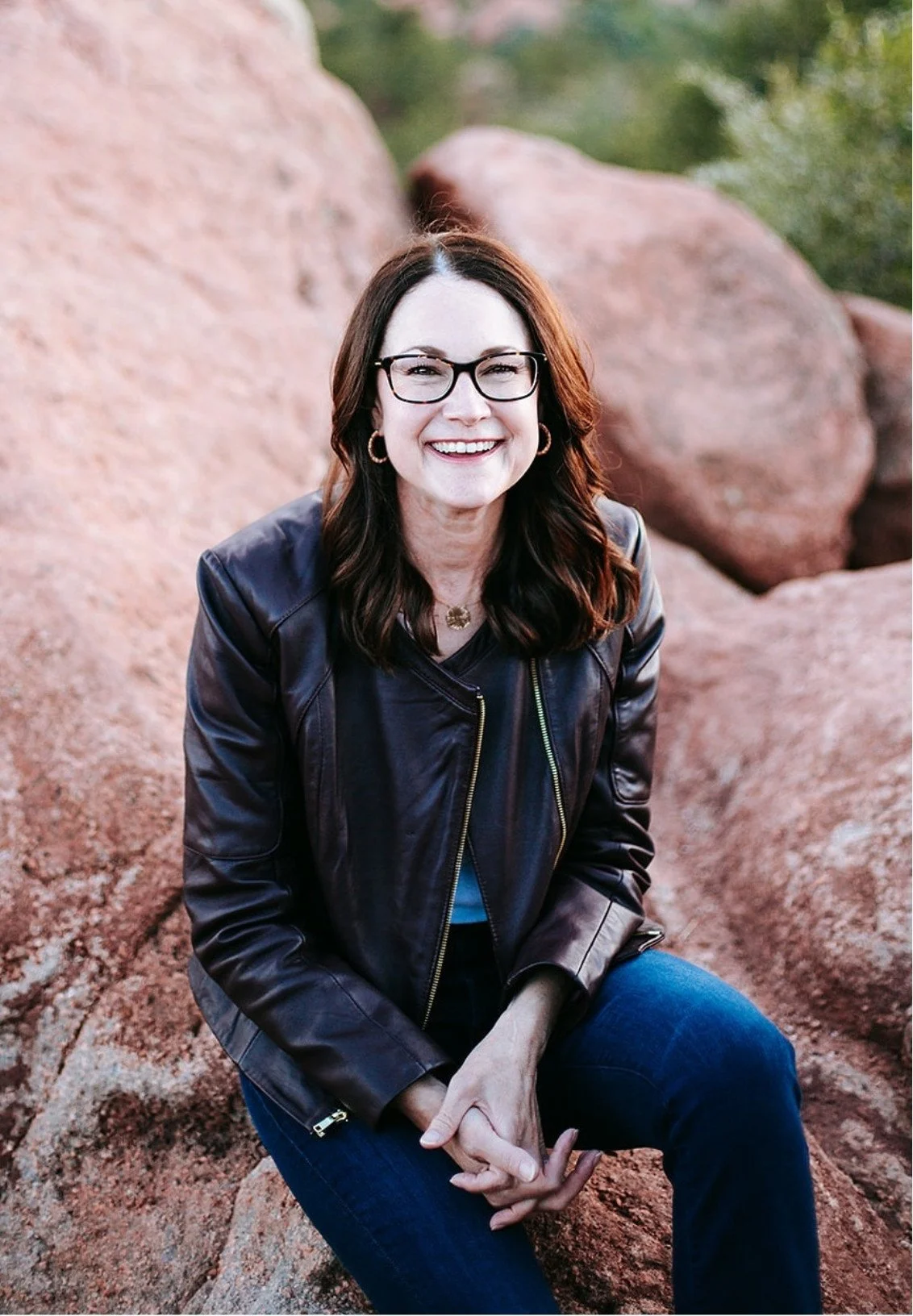 Celia Sugg, Colorado Springs anxiety therapist, sitting on large red rocks outdoors and smiling at the camera.