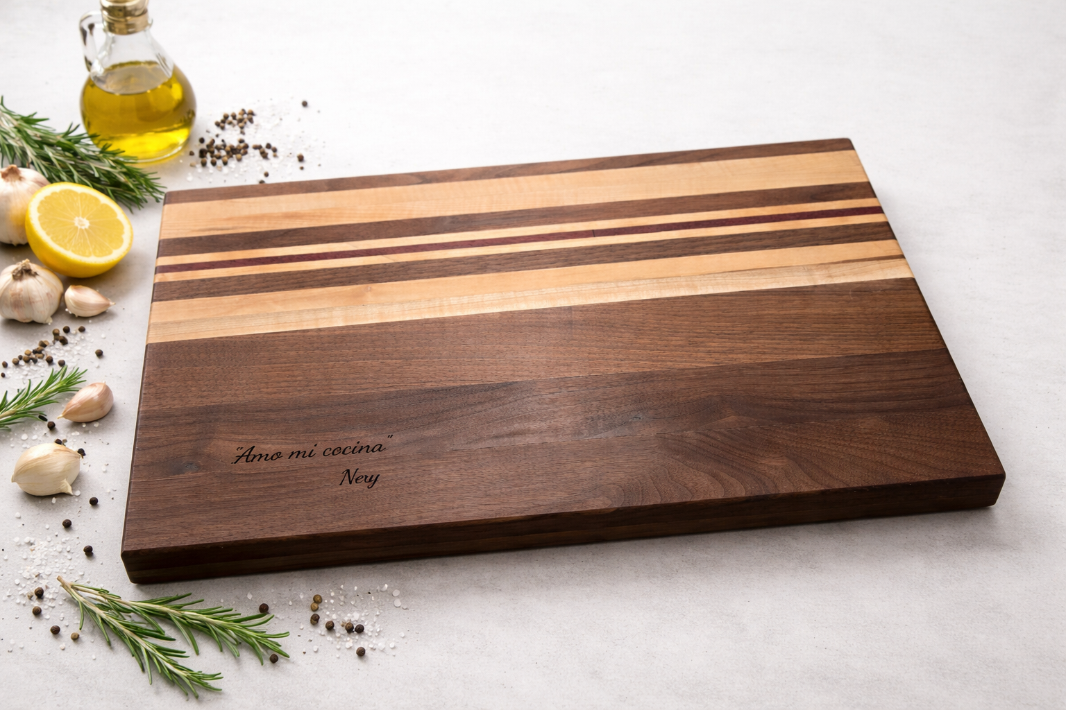 Wooden cutting board with engraved message in Spanish, surrounded by garlic, rosemary, lemon, black pepper, and salt on a white surface.