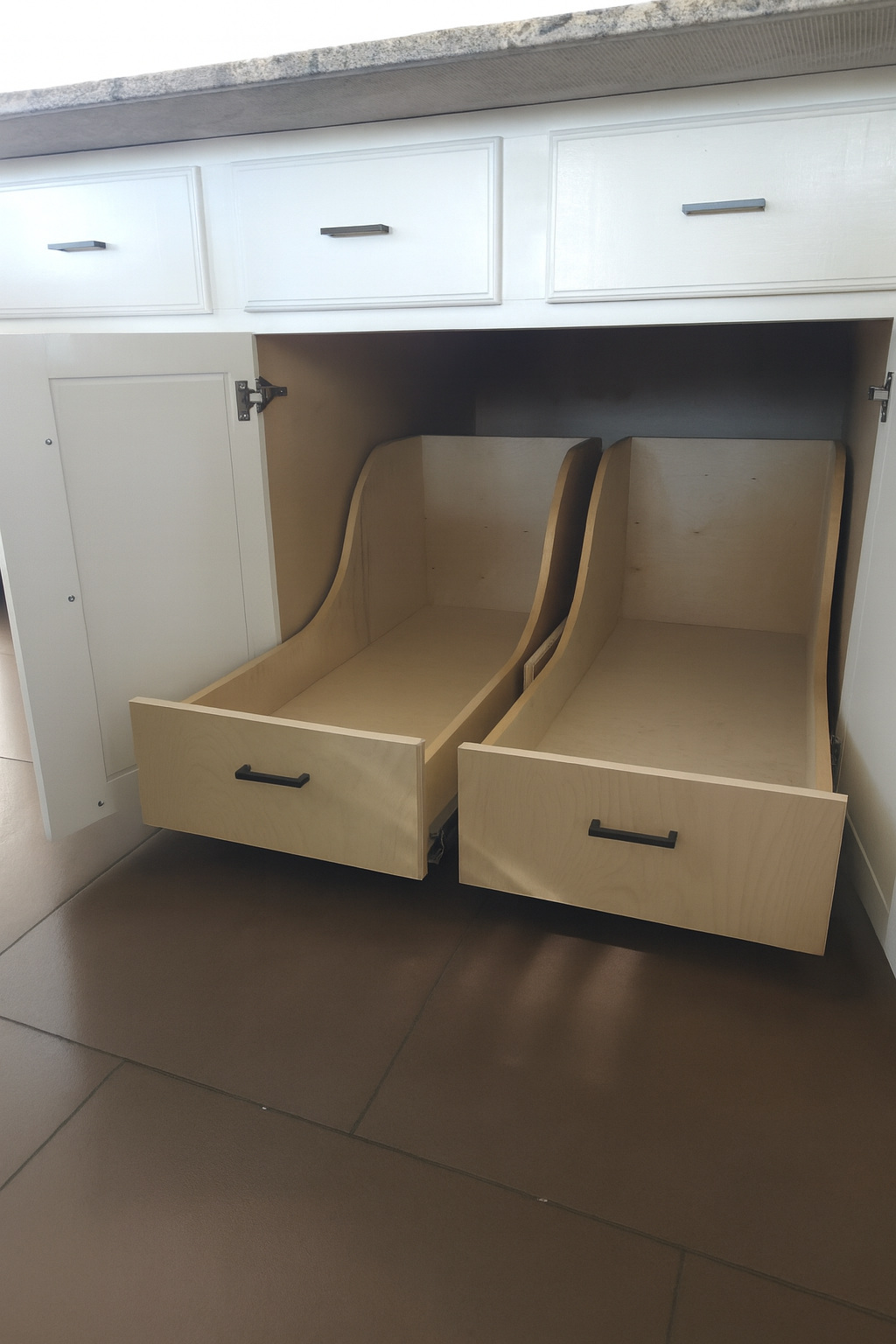 Open kitchen cabinet with custom drawers and white cabinetry with black handles.