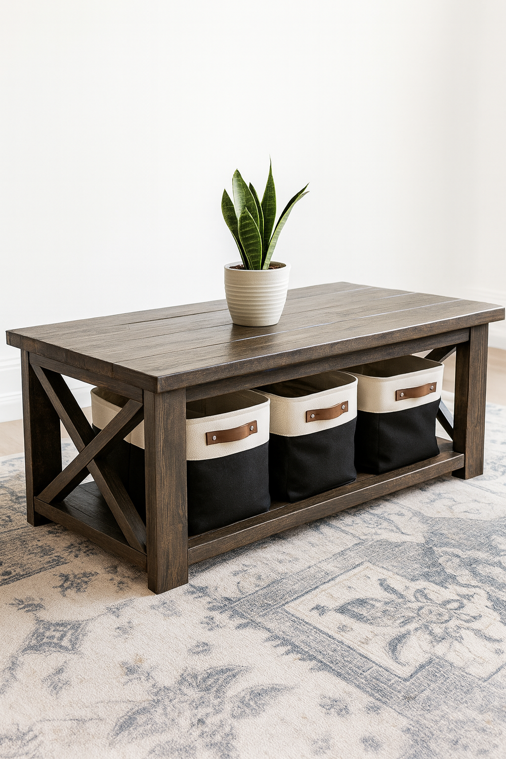 A wooden coffee table with storage baskets underneath, a green leafy plant in a white pot on top, and a light-colored rug on the floor.