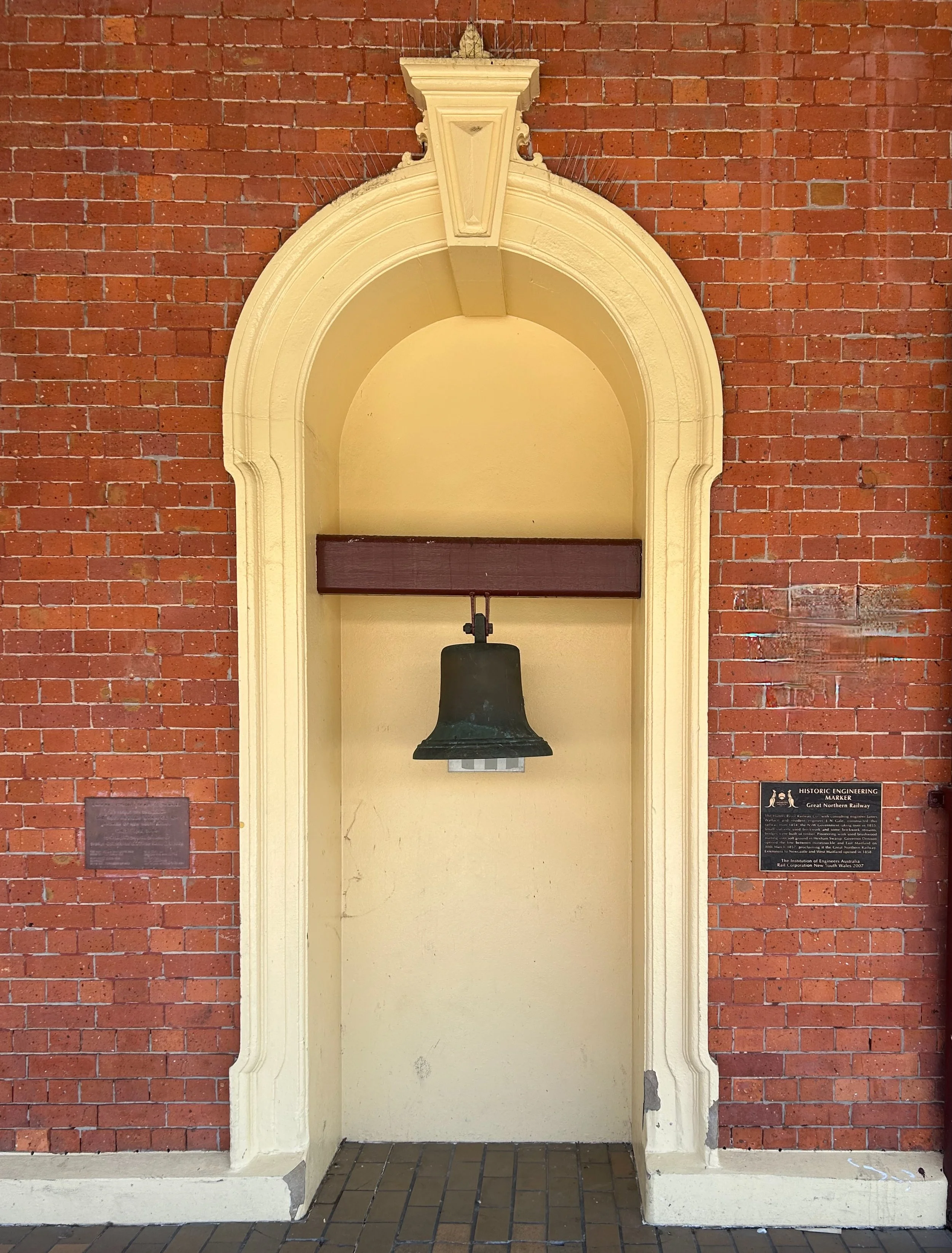 An old church bell inside a decorative arched niche on a brick wall.