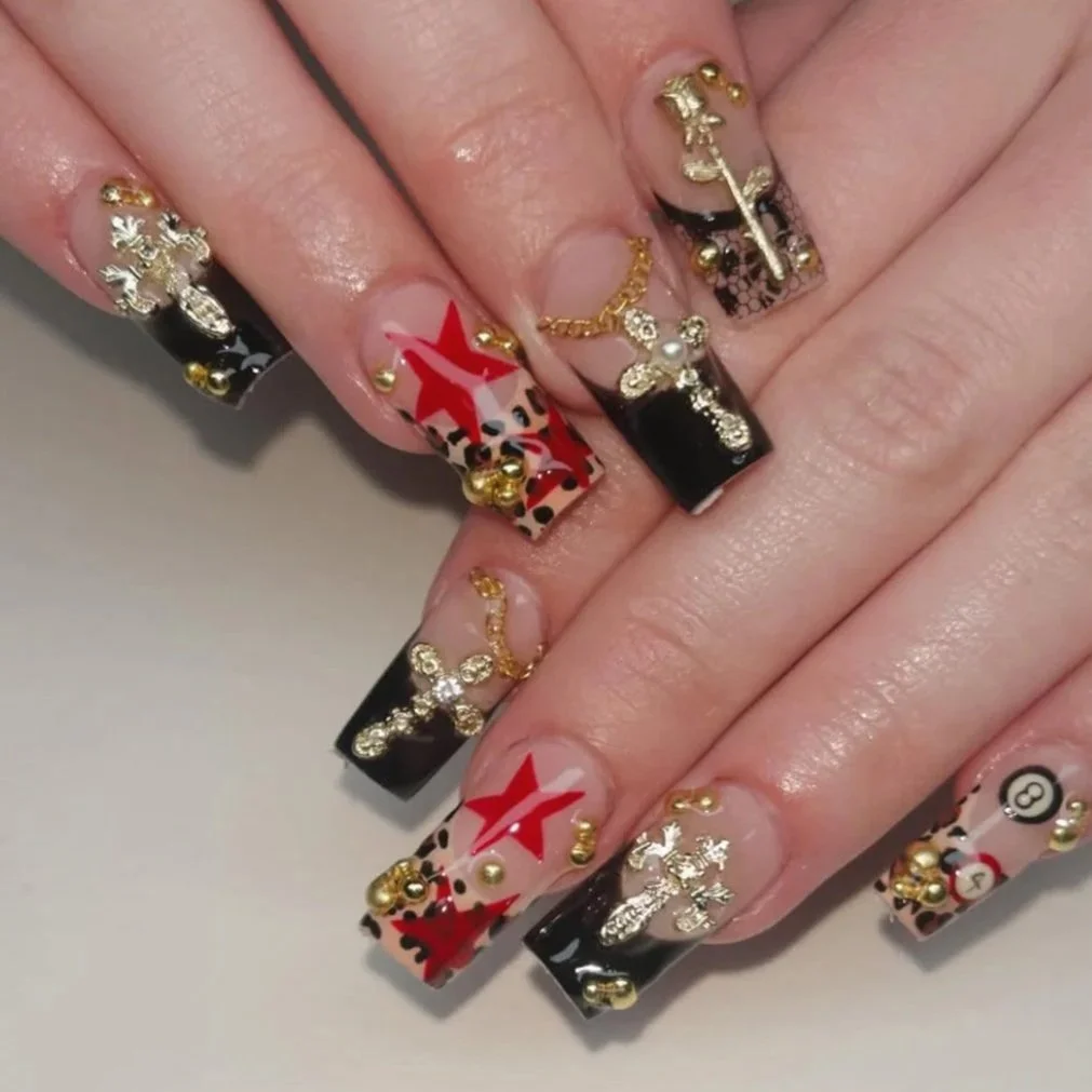 Nail art with leopard print, red star designs, black French tips, and gold and silver embellishments.