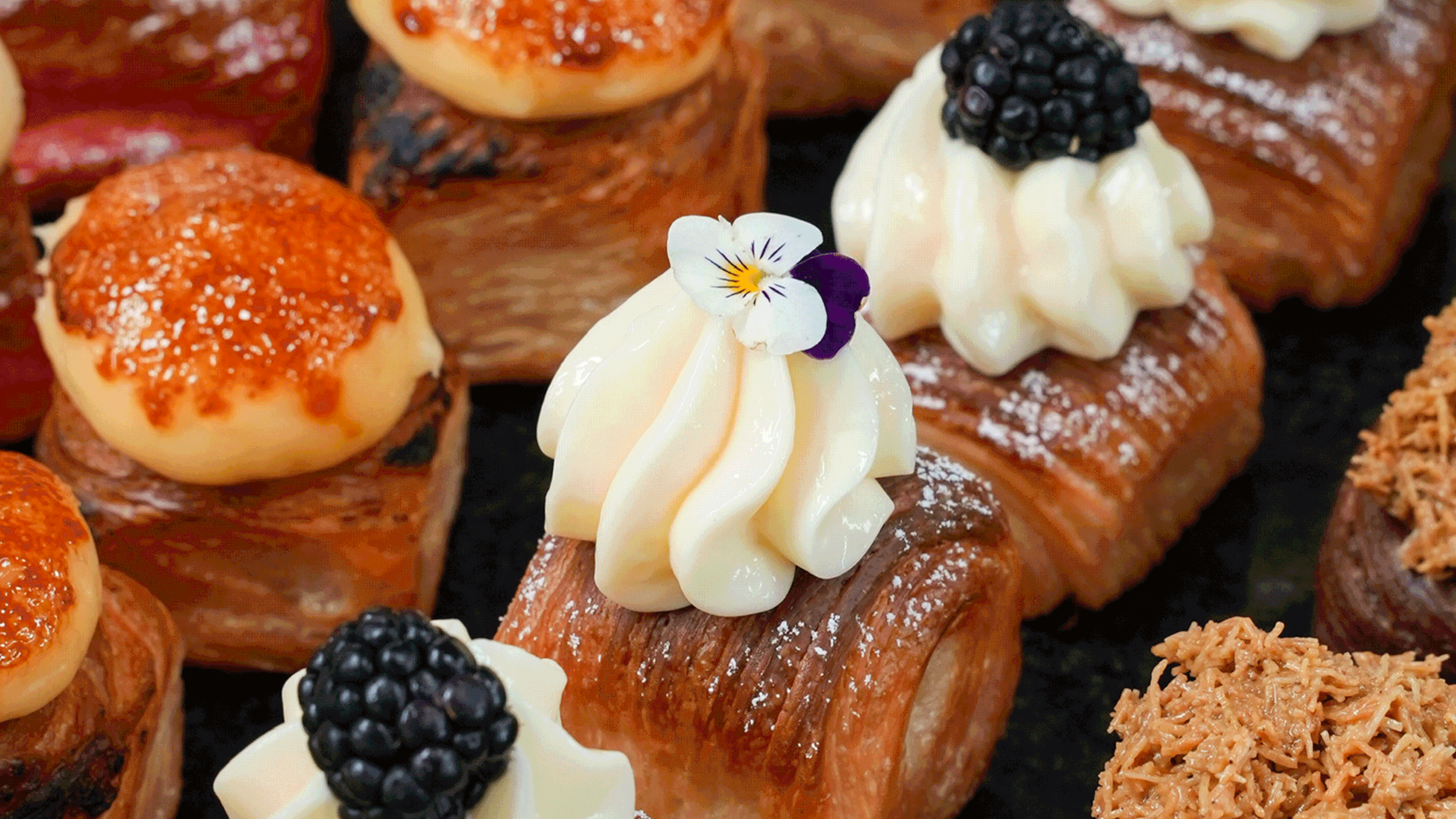 Assorted gourmet pastries decorated with cream, blackberries, edible flowers, and caramelized toppings.