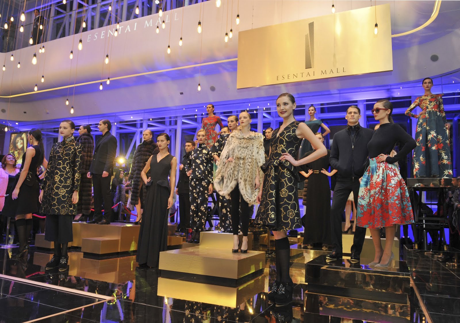 Fashion models posing on a runway during a fashion show at Esentai Mall, with bright lighting and a modern design interior.