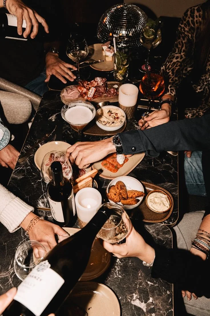 People gathered around a table enjoying drinks, snacks, and appetizers in a dimly lit setting with a disco ball.