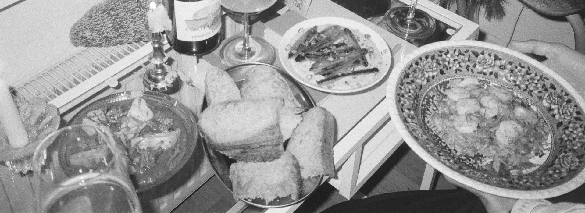 A table filled with various dishes including bread, wine, a salad, and a large bowl of seafood, set in a cozy indoor setting.
