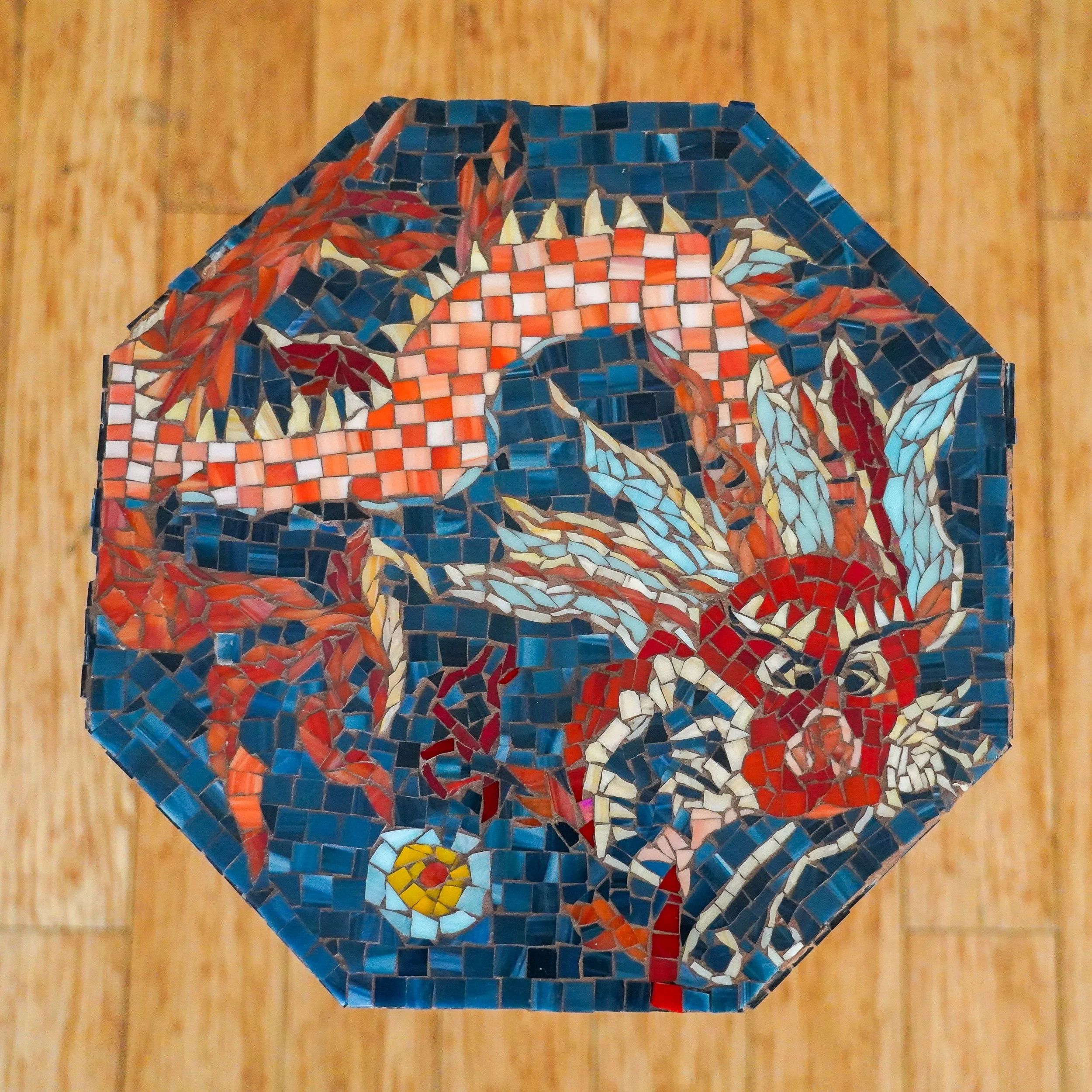 Top view of a decorative mosaic table of a red dragon with detailed features on a wooden floor.
