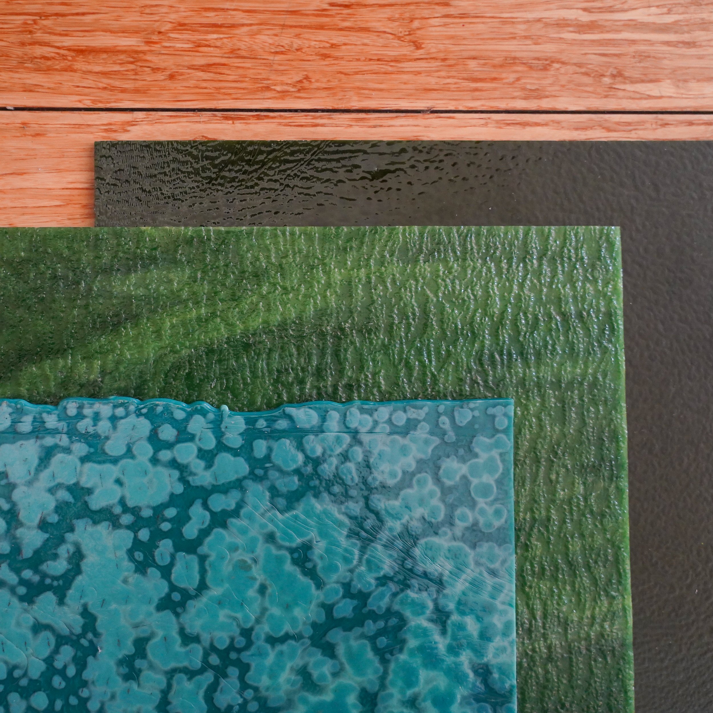 Close-up of three textured sheets of decorative glass in red, black, green, and blue, layered on top of each other.