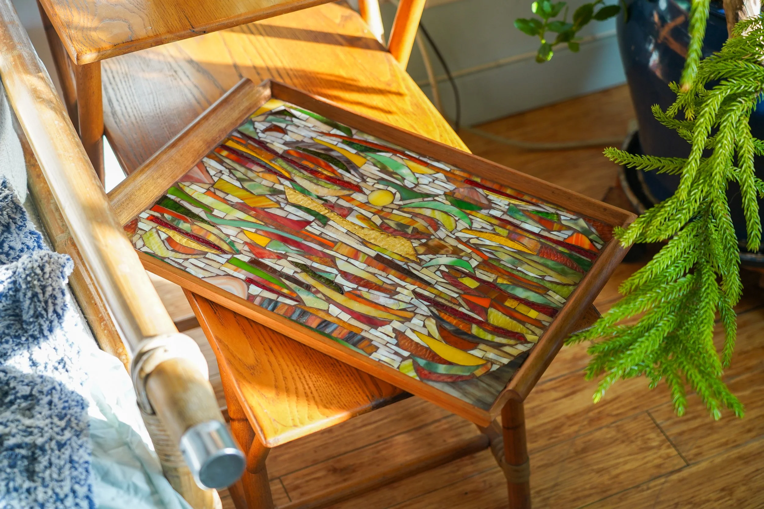 Colorful mosaic artwork in a wooden frame on a small wooden chair.
