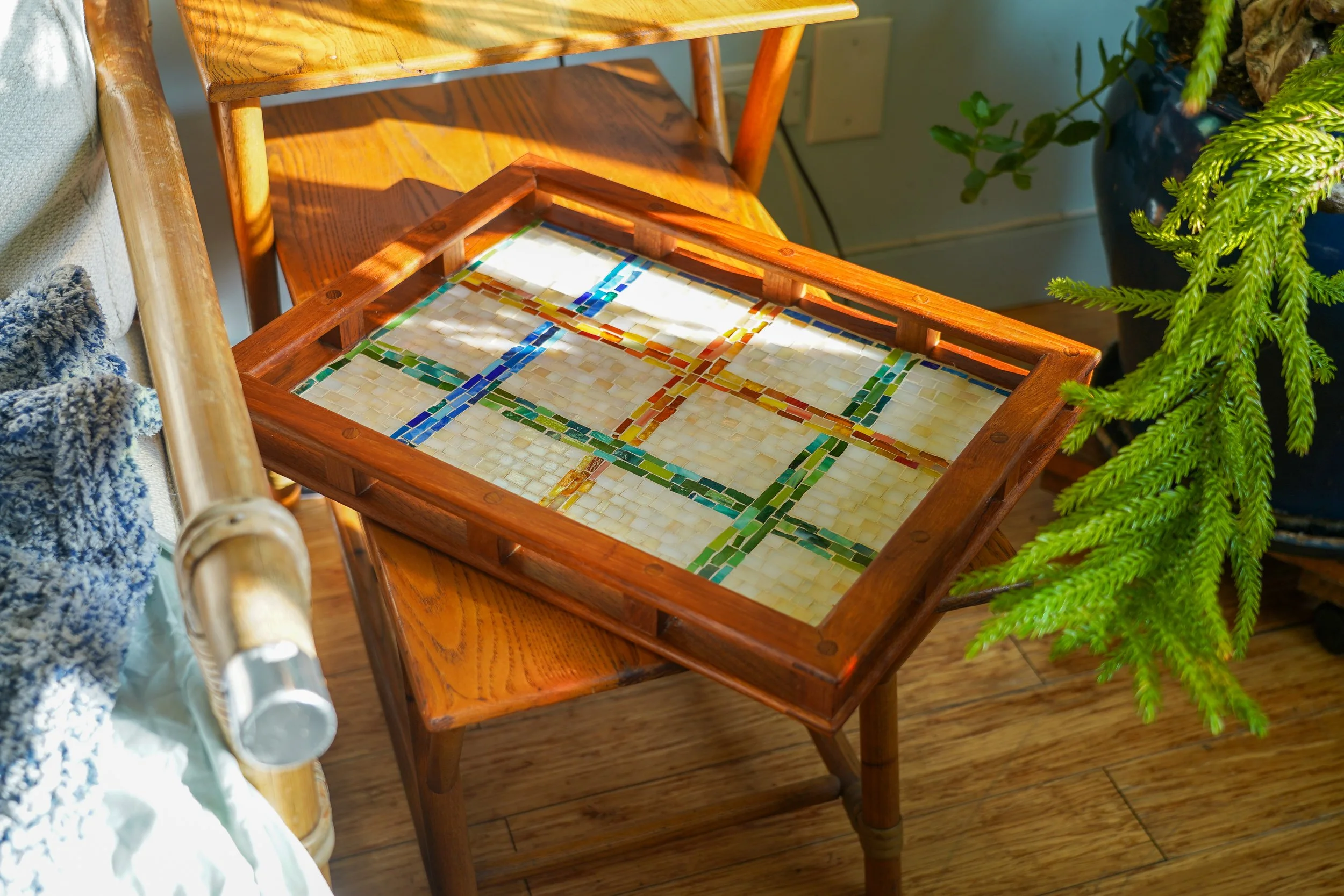 A wooden tray with a mosaic pattern of colored tiles, placed on a wooden table.