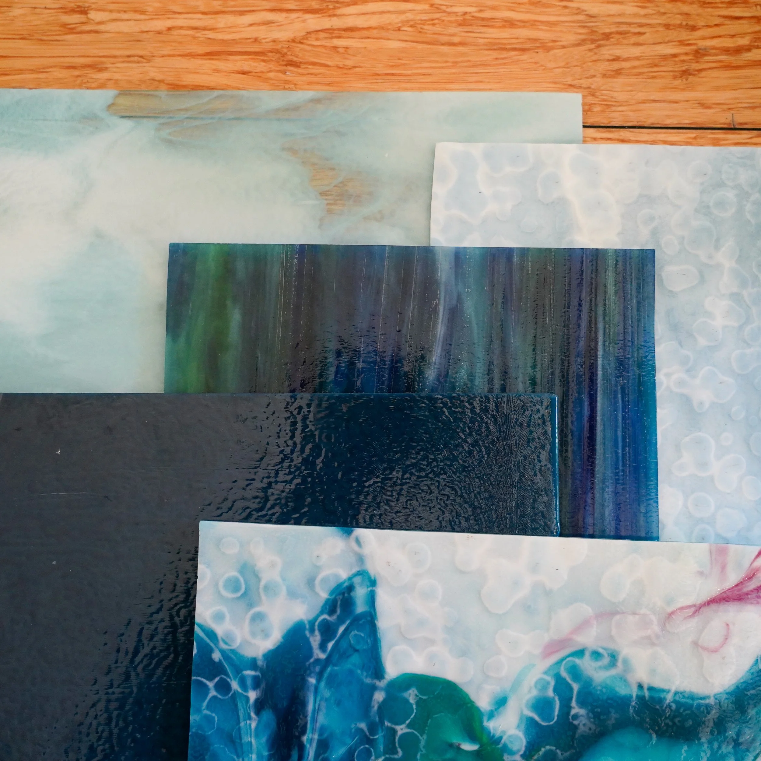 Multiple colorful acrylic sheets with various textures and patterns, placed on a wooden surface.