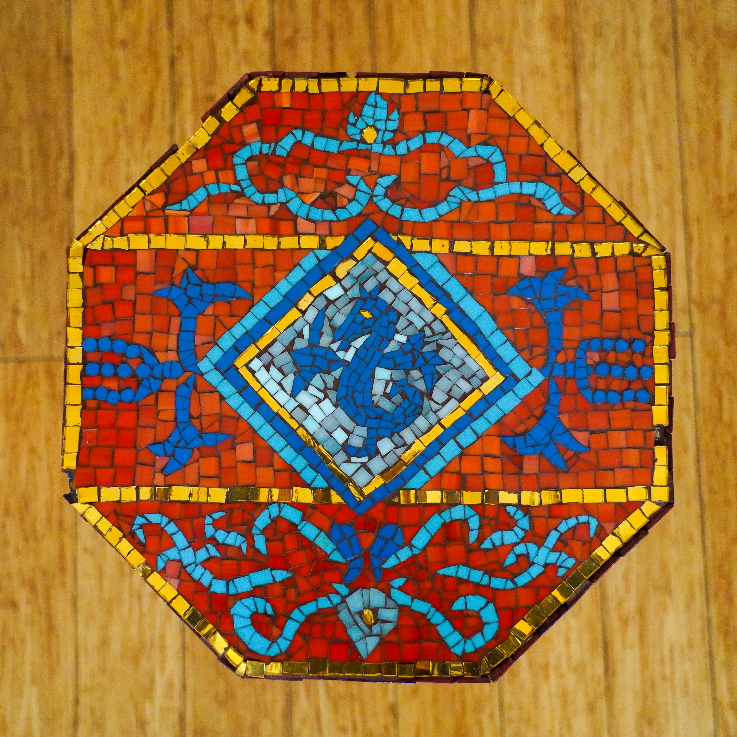 Top view of a decorative mosaic table with red, blue, and yellow pattern with a blue dragon in the middle.