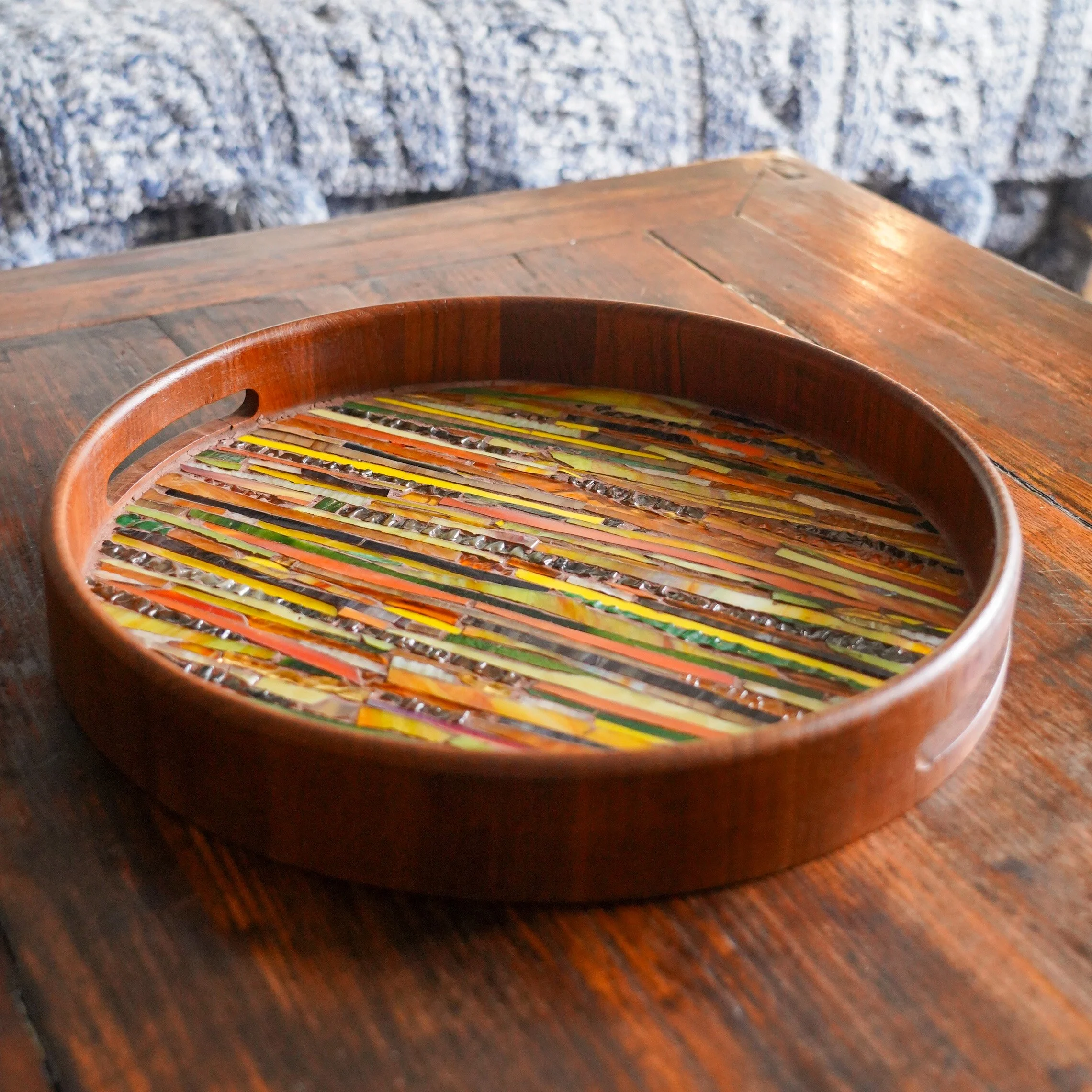 Colorful mosaic art in a round wooden frame on a wooden surface.